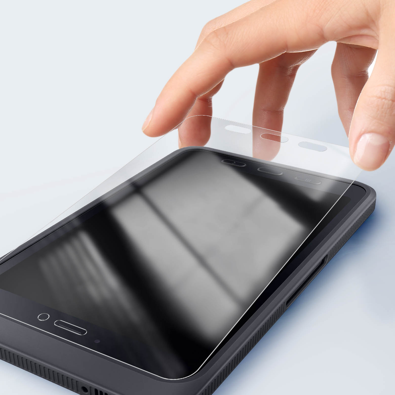 Una mano applica una protezione per lo schermo su uno smartphone nero. Il telefono è su una superficie chiara. La protezione è trasparente.