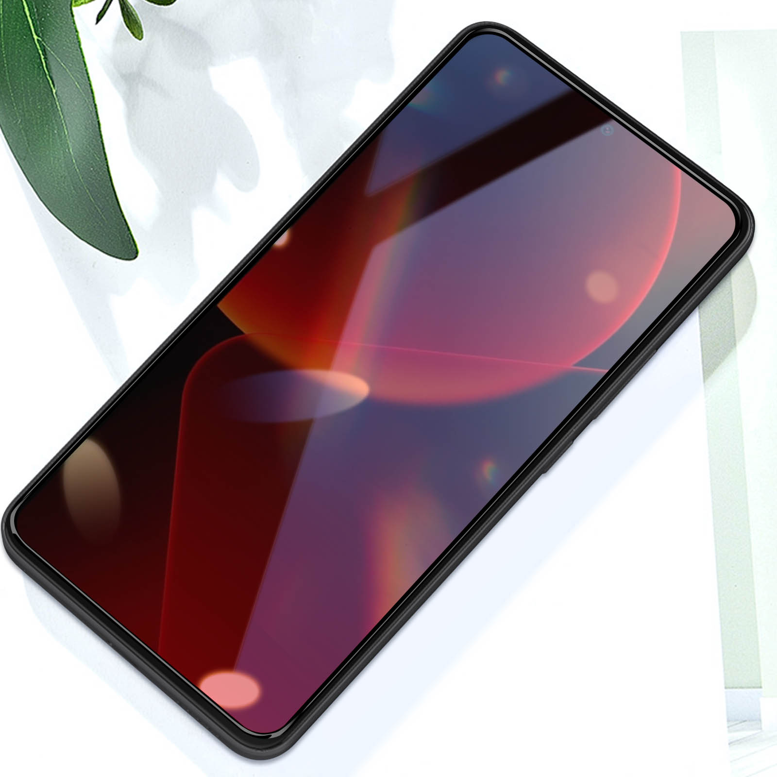 Schermo del telefono che riflette tonalità rosse, cornice nera, su superficie bianca con foglia verde.