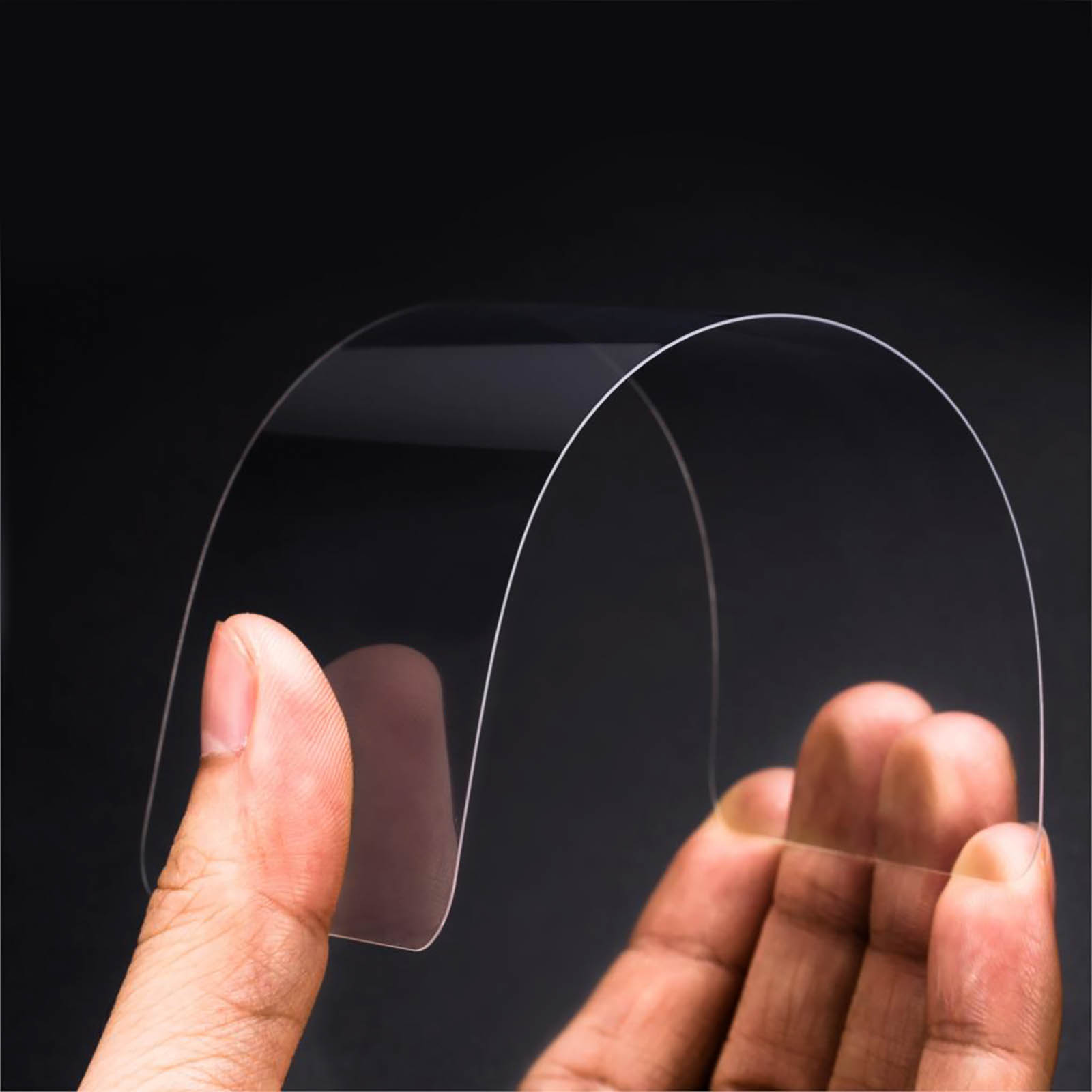 Mano che tiene un pezzo curvo e trasparente di plastica su sfondo scuro. Dita visibili.