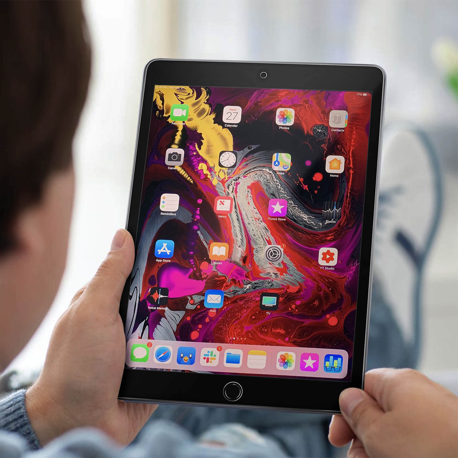Una persona tiene in mano un iPad che mostra icone di app. Lo schermo mostra uno sfondo colorato. La persona è sfocata.