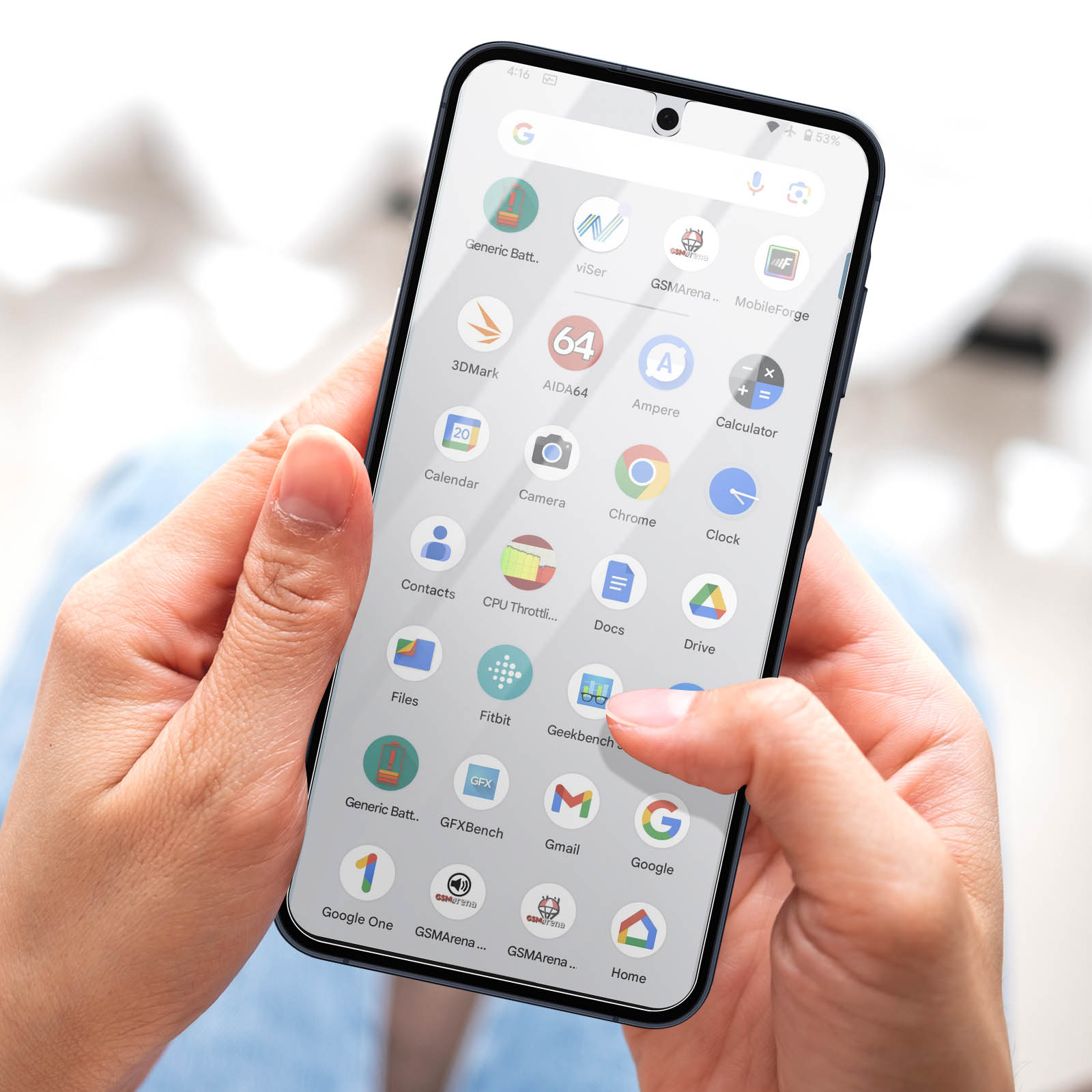 Una mano tiene in mano uno smartphone che mostra icone di app. Il dito tocca l'icona di Geekbench. Lo schermo mostra varie icone di app.