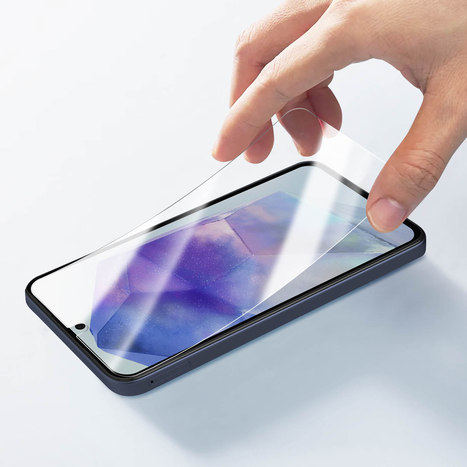 Una mano applica una protezione schermo a uno smartphone blu scuro. Lo sfondo è chiaro e neutro.