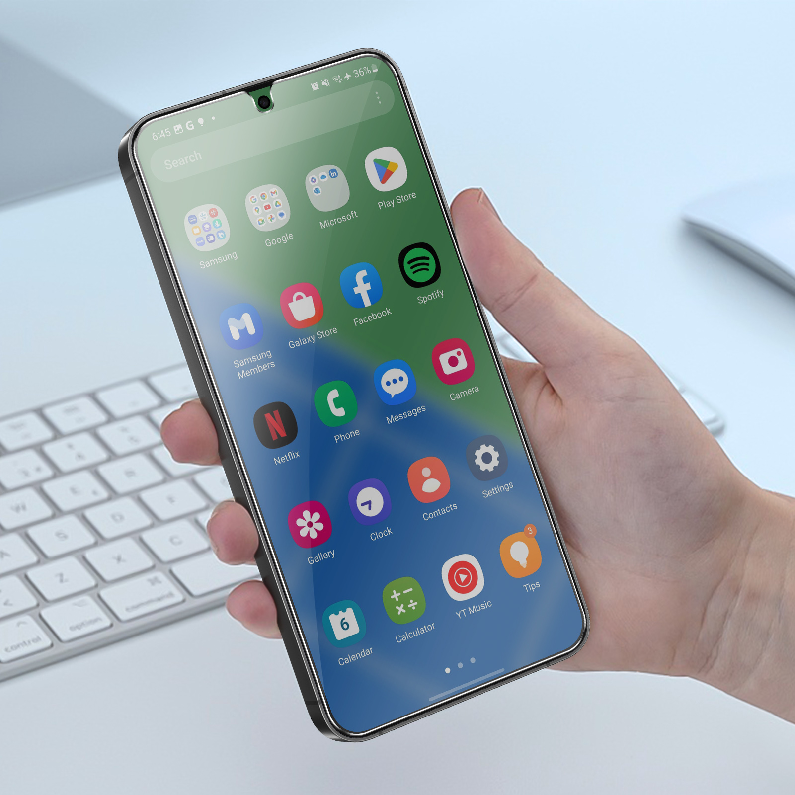 Una mano che tiene uno smartphone con icone di app. Sullo sfondo una tastiera e una superficie bianca.