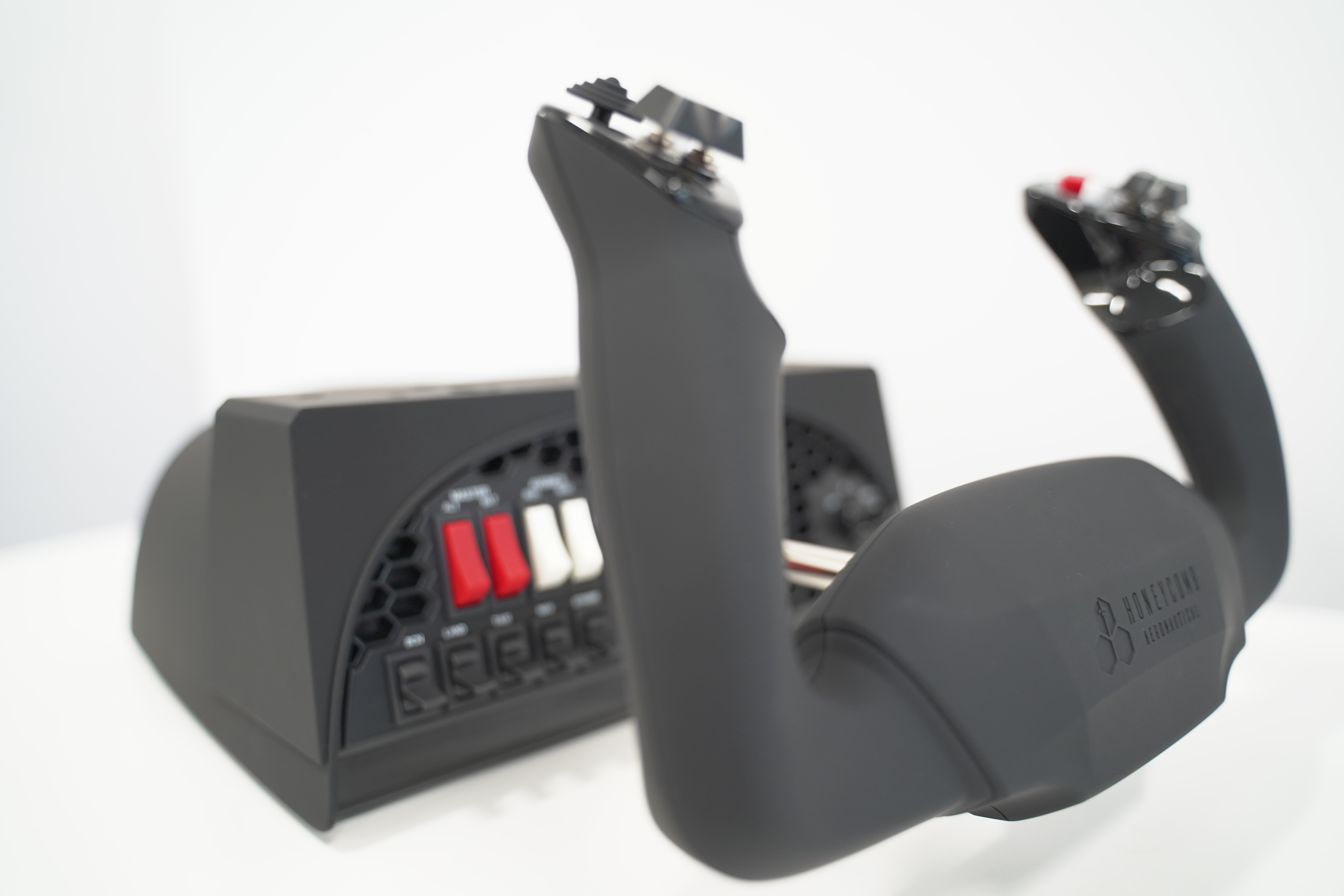 A black flight yoke with buttons and a panel with switches. The yoke has a logo that reads Honeycomb Aeronautical.