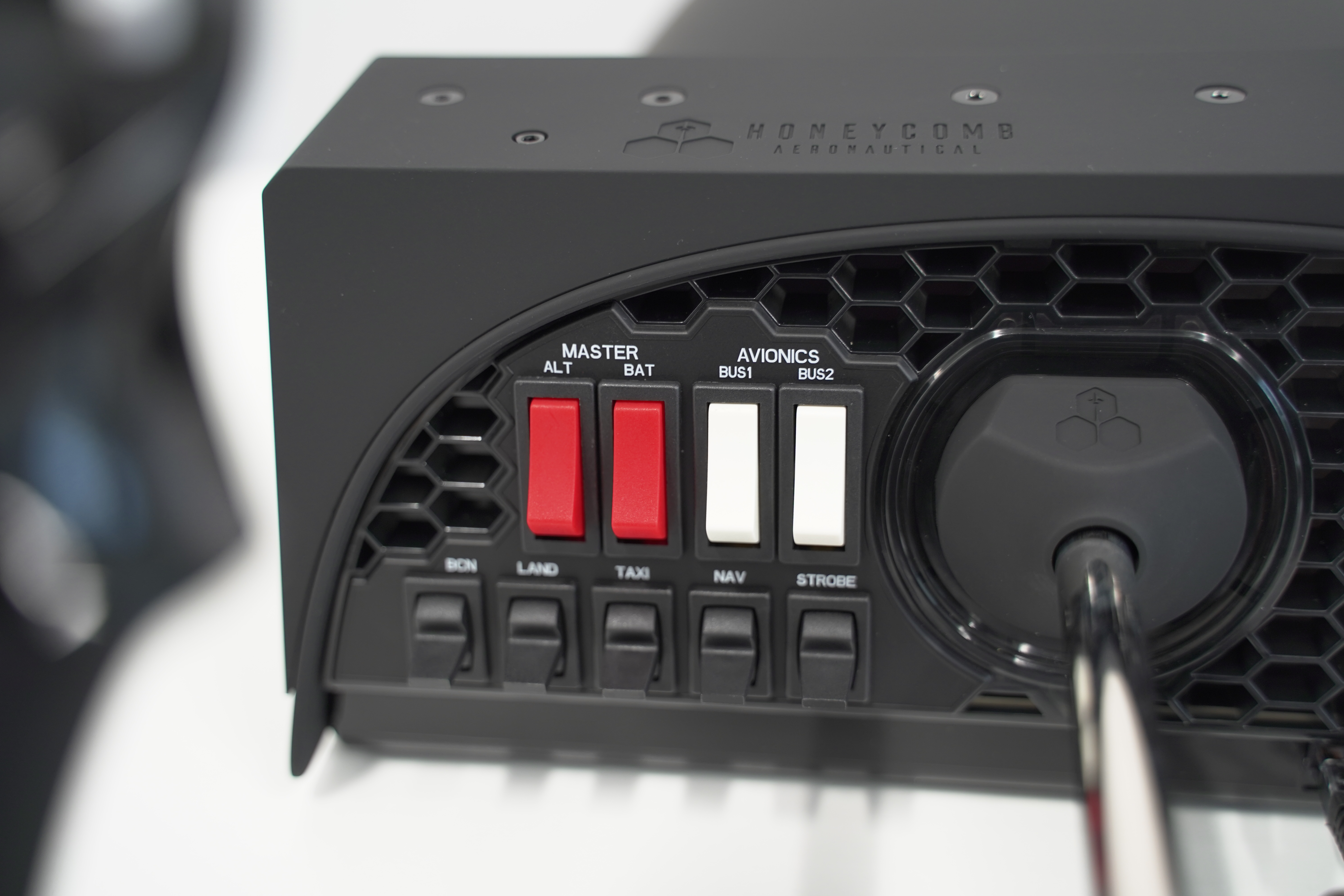 A black control panel with red and white switches. The Honeycomb Aeronautical logo is visible. A silver stick extends.