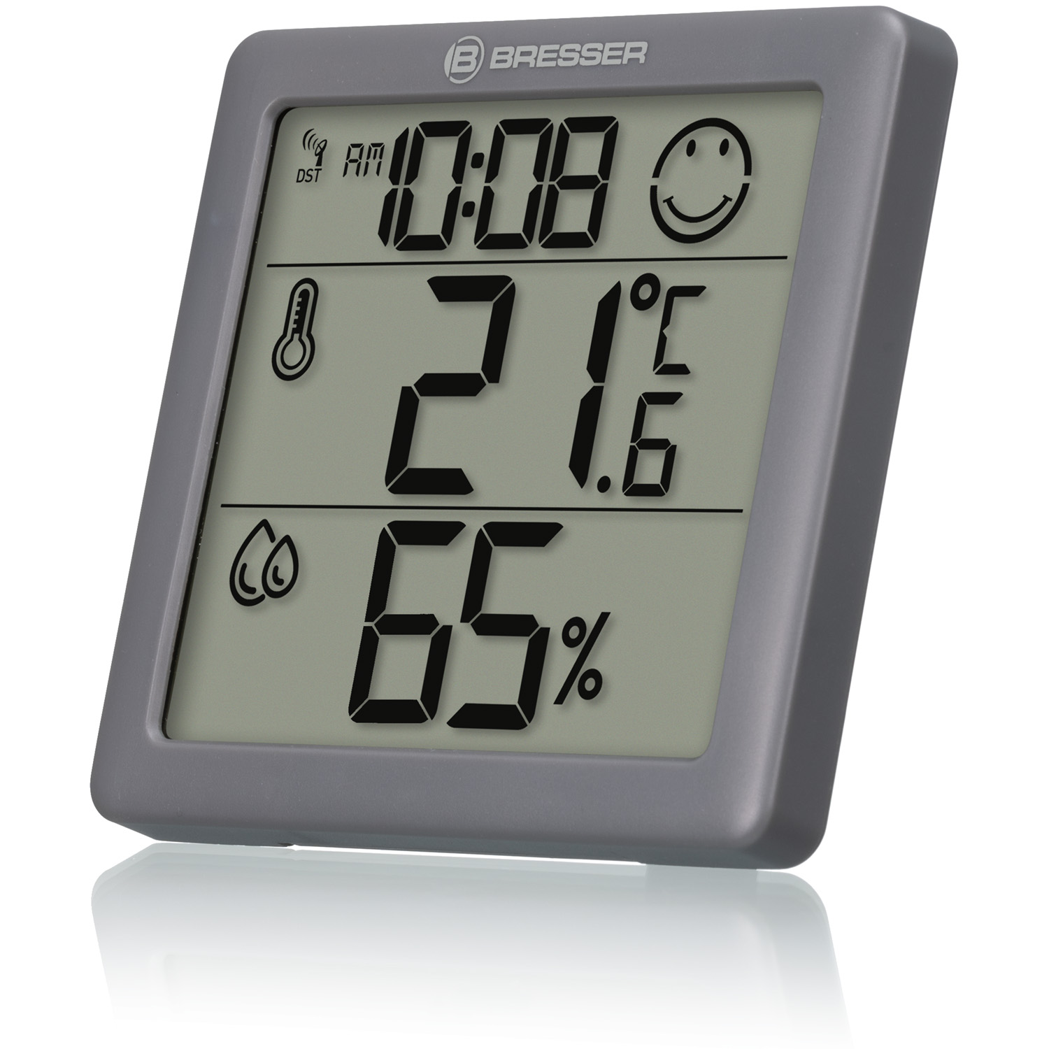 Una estación meteorológica digital gris muestra la hora, la temperatura (21,6°C) y la humedad (65%). Tiene un icono de cara sonriente.