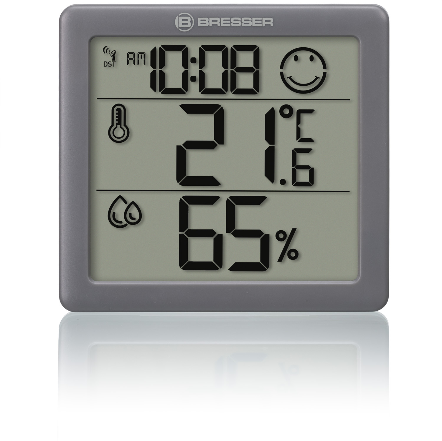 Una pantalla digital gris Bresser muestra la hora, la temperatura y la humedad. Tiene una carita sonriente e iconos de temperatura y humedad.