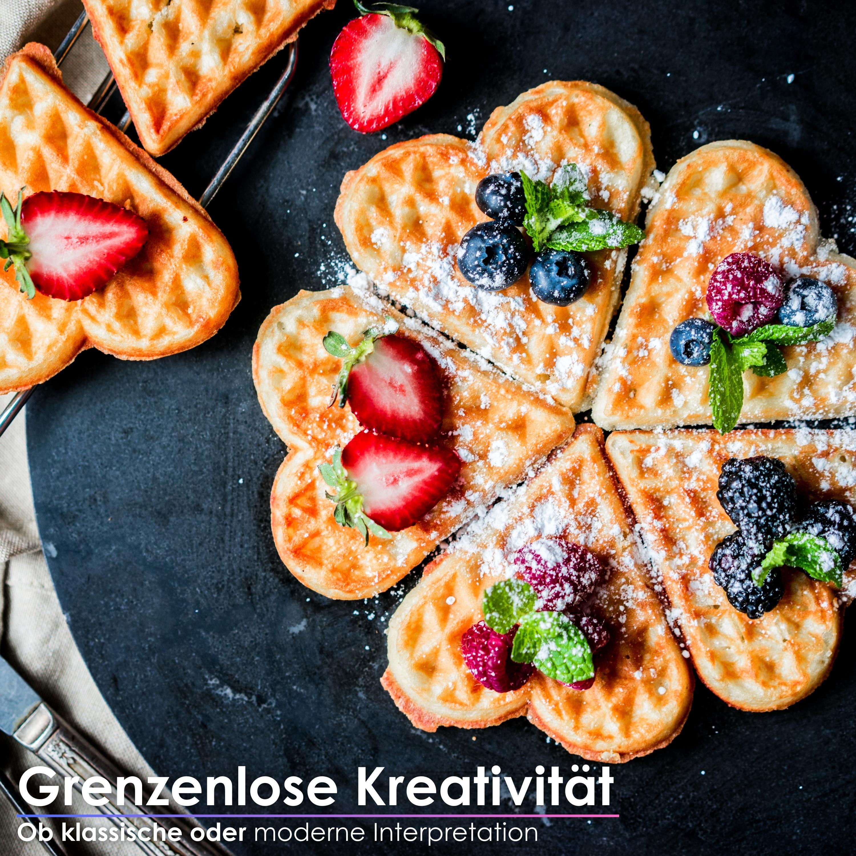 Herzförmige Waffeln mit Beeren und Puderzucker auf schwarzem Untergrund. Erdbeeren, Blaubeeren und Himbeeren.