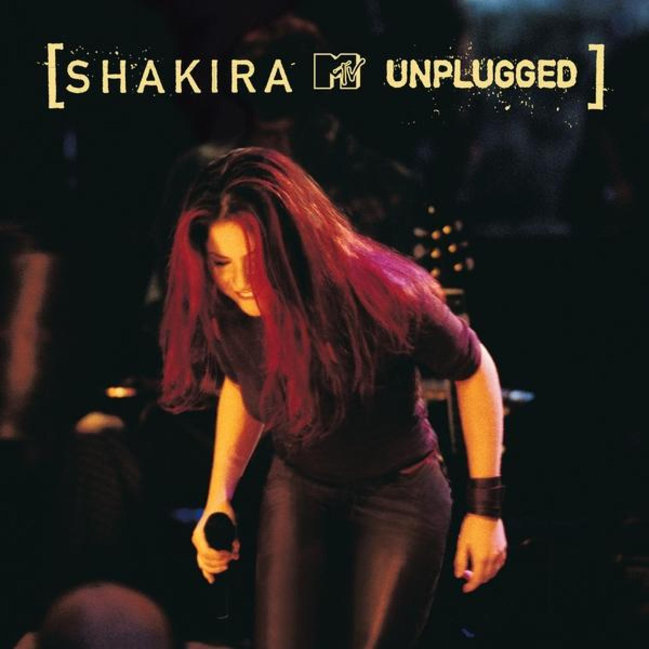 Shakira sul palco, capelli rossi, con un microfono. Logo MTV Unplugged in alto. Sfondo scuro, luci del palco.