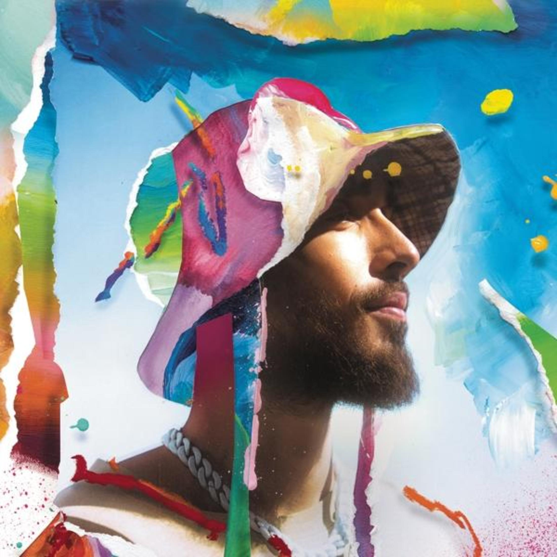 Un uomo con un cappello e una collana colorati, su uno sfondo astratto con spruzzi blu, gialli e rosa.