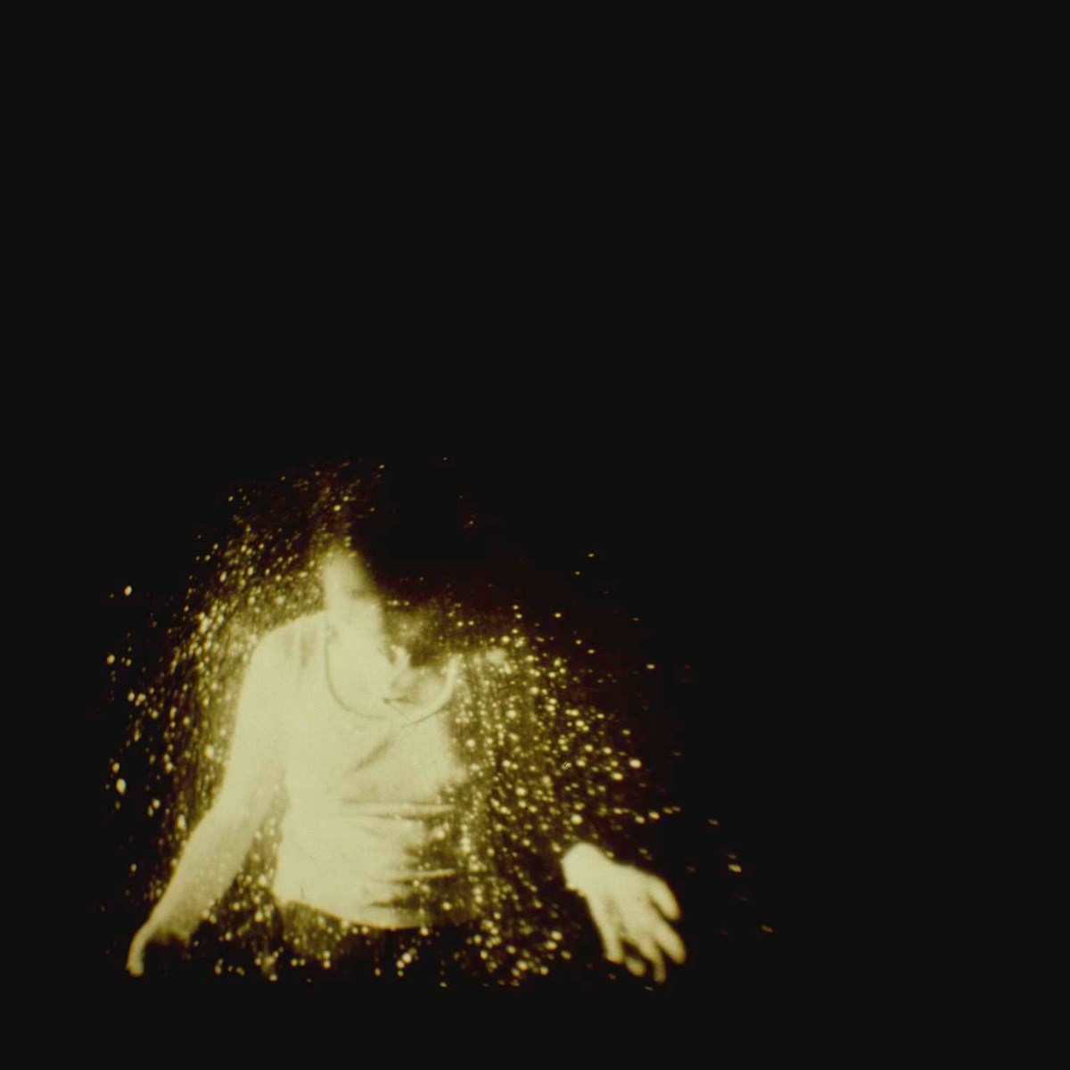 Si vede una persona, illuminata da una luce dorata. La figura è circondata da uno spruzzo di particelle dorate su sfondo nero.