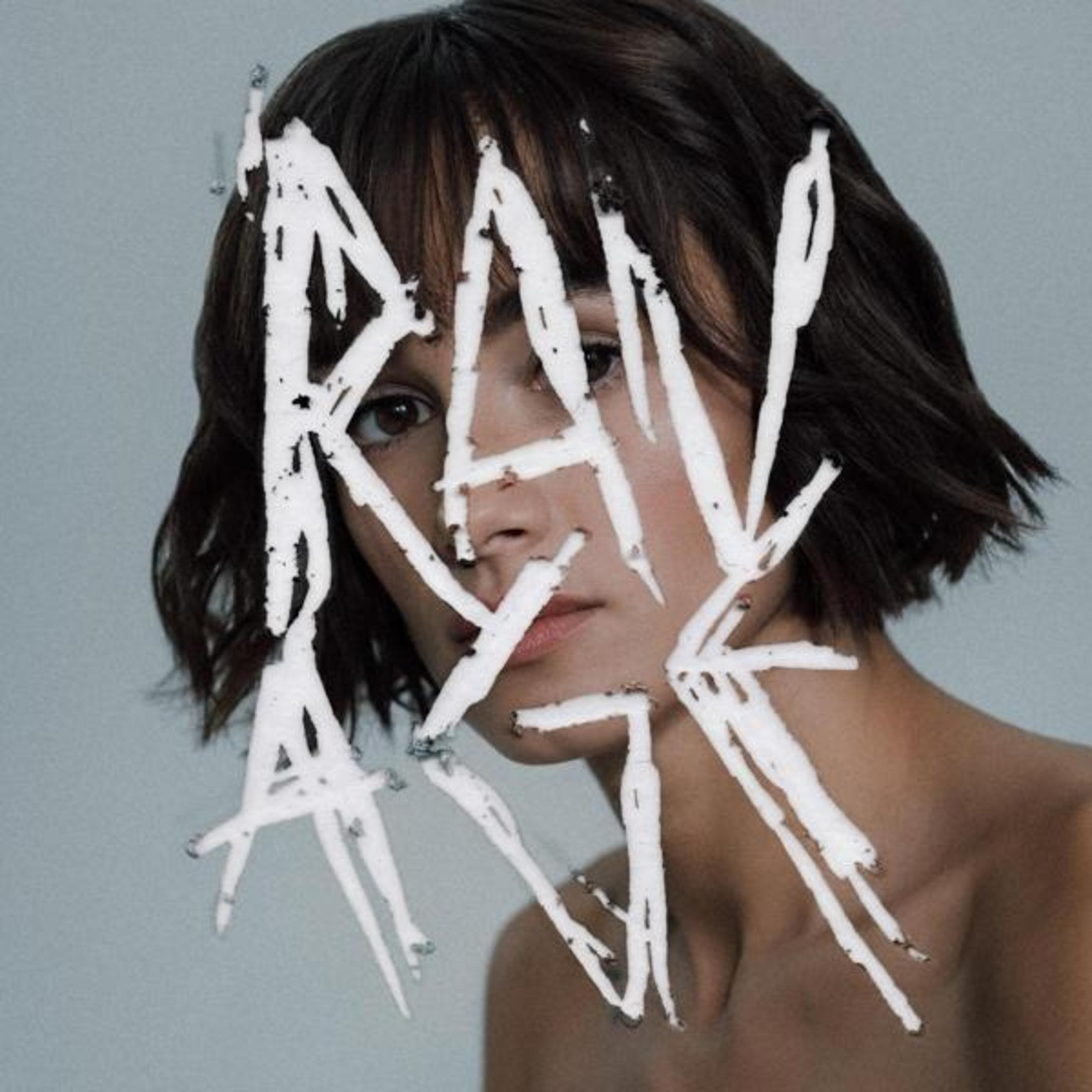 Il volto di una donna con la parola 'RAW ART' in vernice bianca. Ha i capelli scuri e guarda la fotocamera.