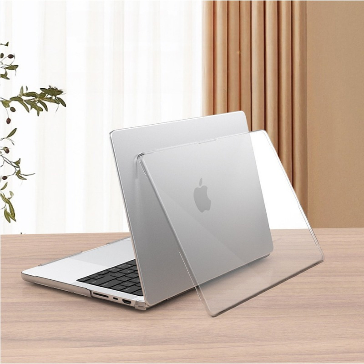 Ein silbernes MacBook mit einer durchsichtigen Schutzhülle steht auf einem Holztisch. Hintergrund: Vorhänge, Licht und eine Pflanze.