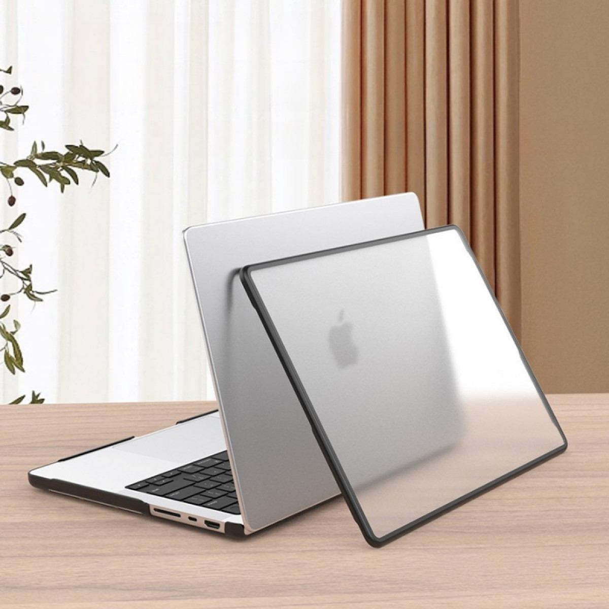 Silberner Laptop mit schwarzer Tastatur und Schutzhülle auf einem Holztisch. Vorhänge und Pflanze im Hintergrund.
