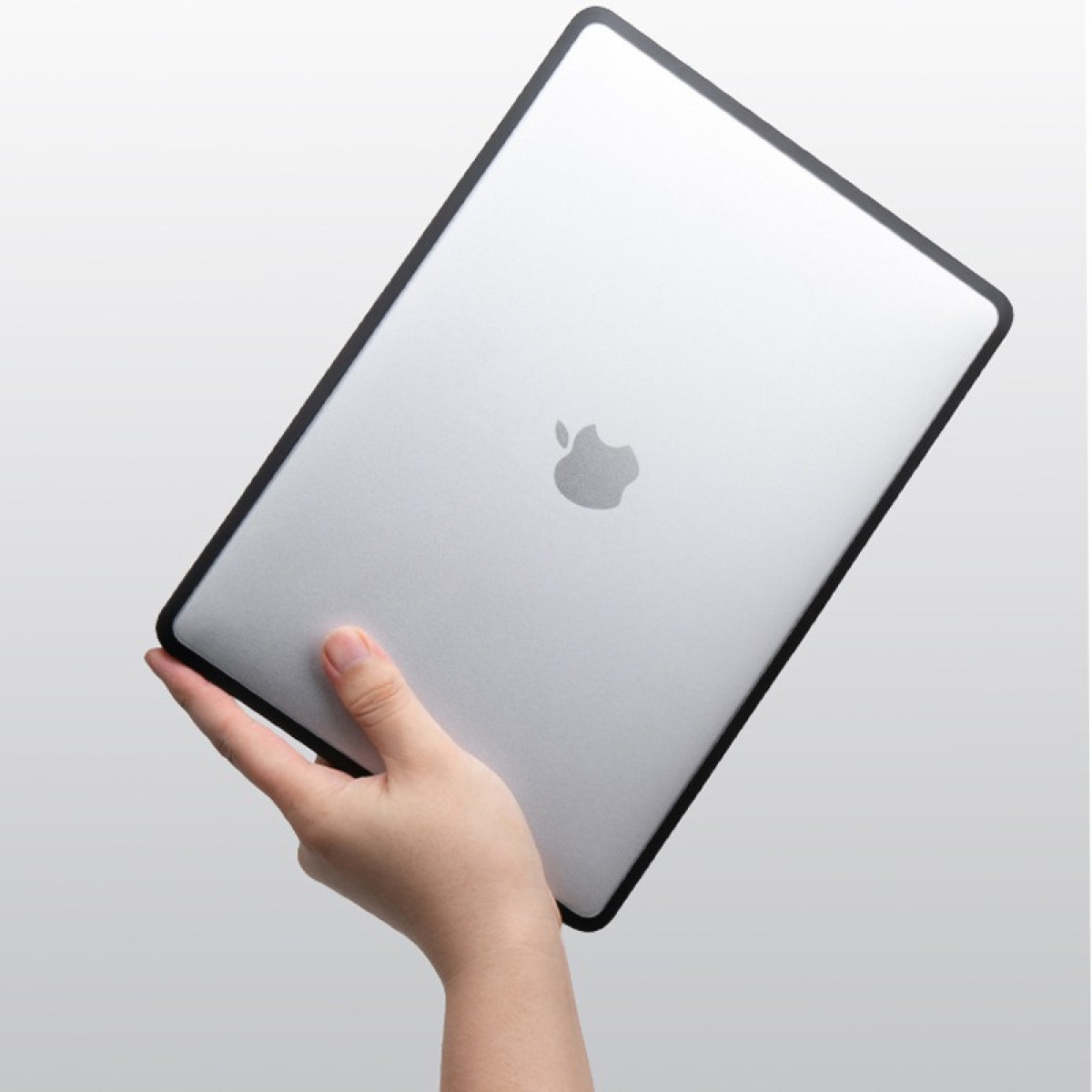 Eine Hand hält einen silbernen Laptop mit einem Apple-Logo. Der Laptop hat einen schwarzen Rahmen. Der Hintergrund ist ein weißer Farbverlauf.