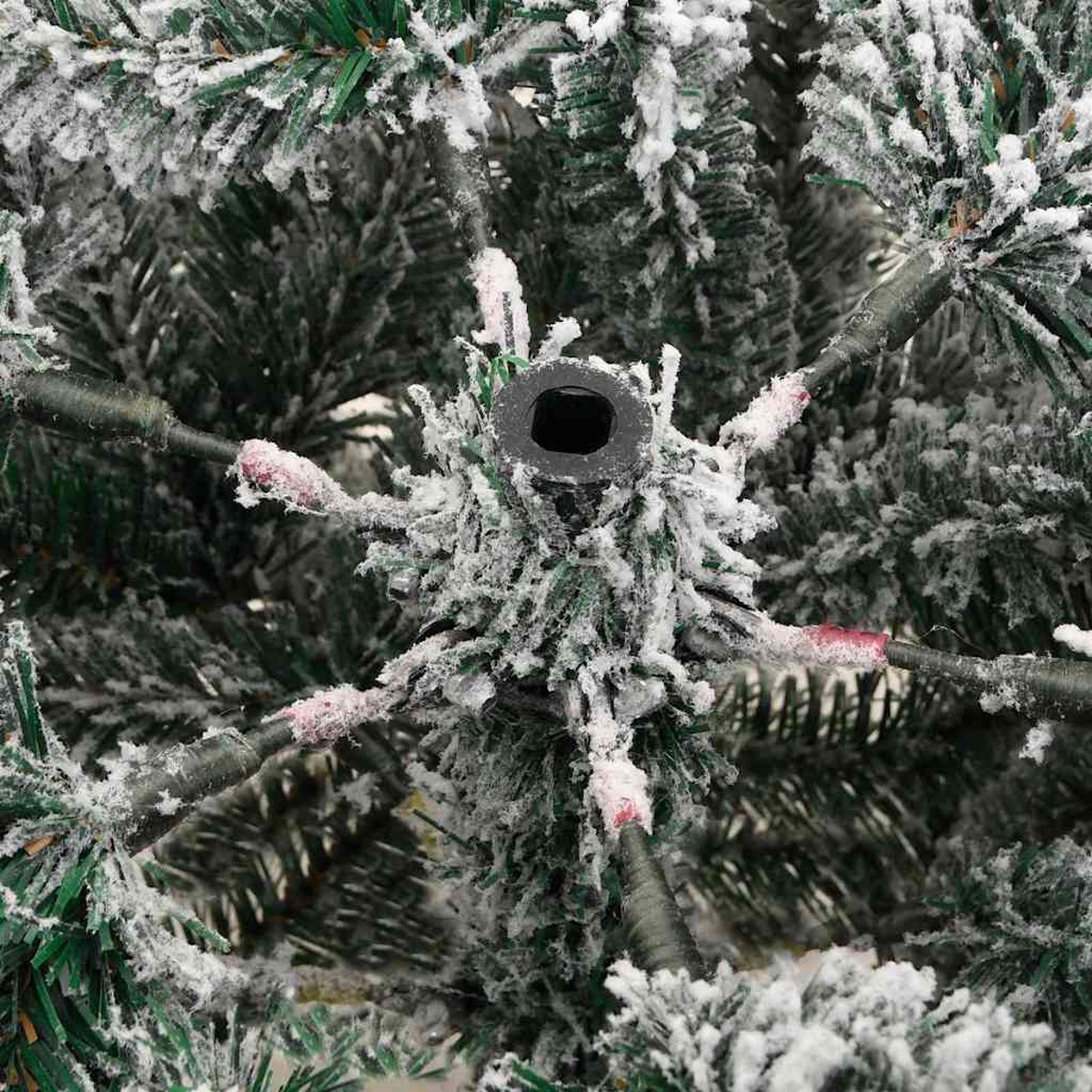 Nahaufnahme eines verschneiten Weihnachtsbaums. Grüne Nadeln mit weißem Schnee. Schwarze Stange in der Mitte. Äste mit roten und schwarzen Details.