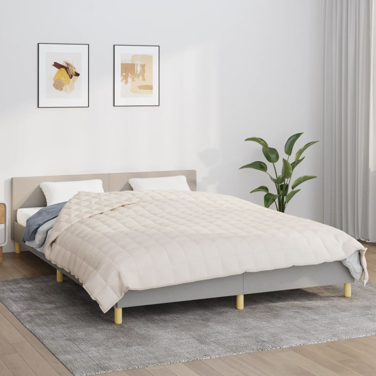 Ein Bett mit einem beigen Steppbett. Zwei gerahmte abstrakte Kunstwerke hängen darüber. Rechts ist eine grüne Pflanze. Auf dem Boden liegt ein grauer Teppich.