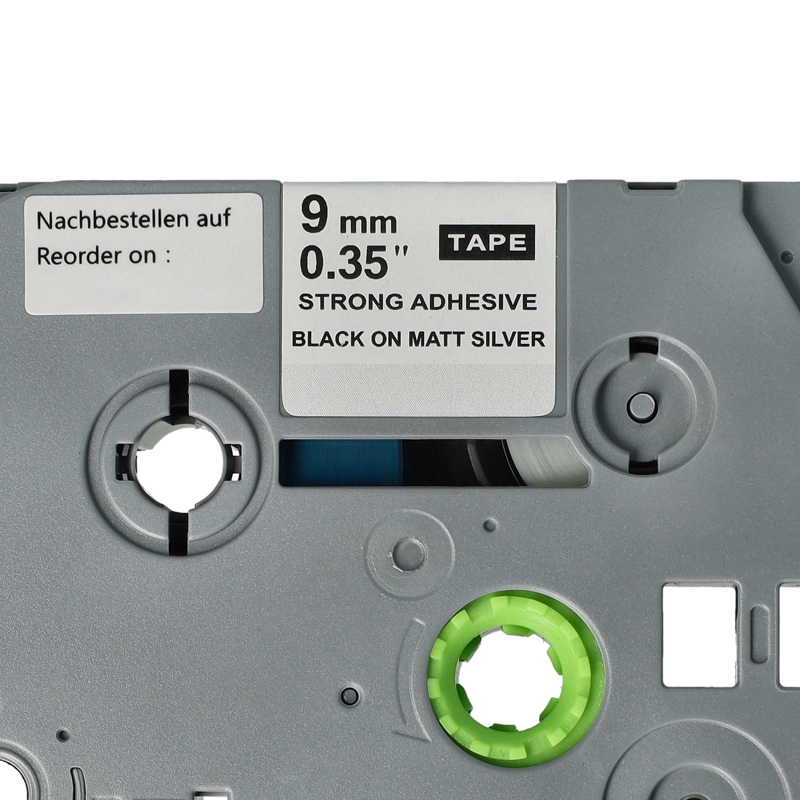 Nahaufnahme des Etikettenbands. Text: 9 mm, 0,35 Zoll, STARKER KLEBSTOFF, SCHWARZ AUF MATT-SILBER. Grünes Rad und grauer Kunststoff.