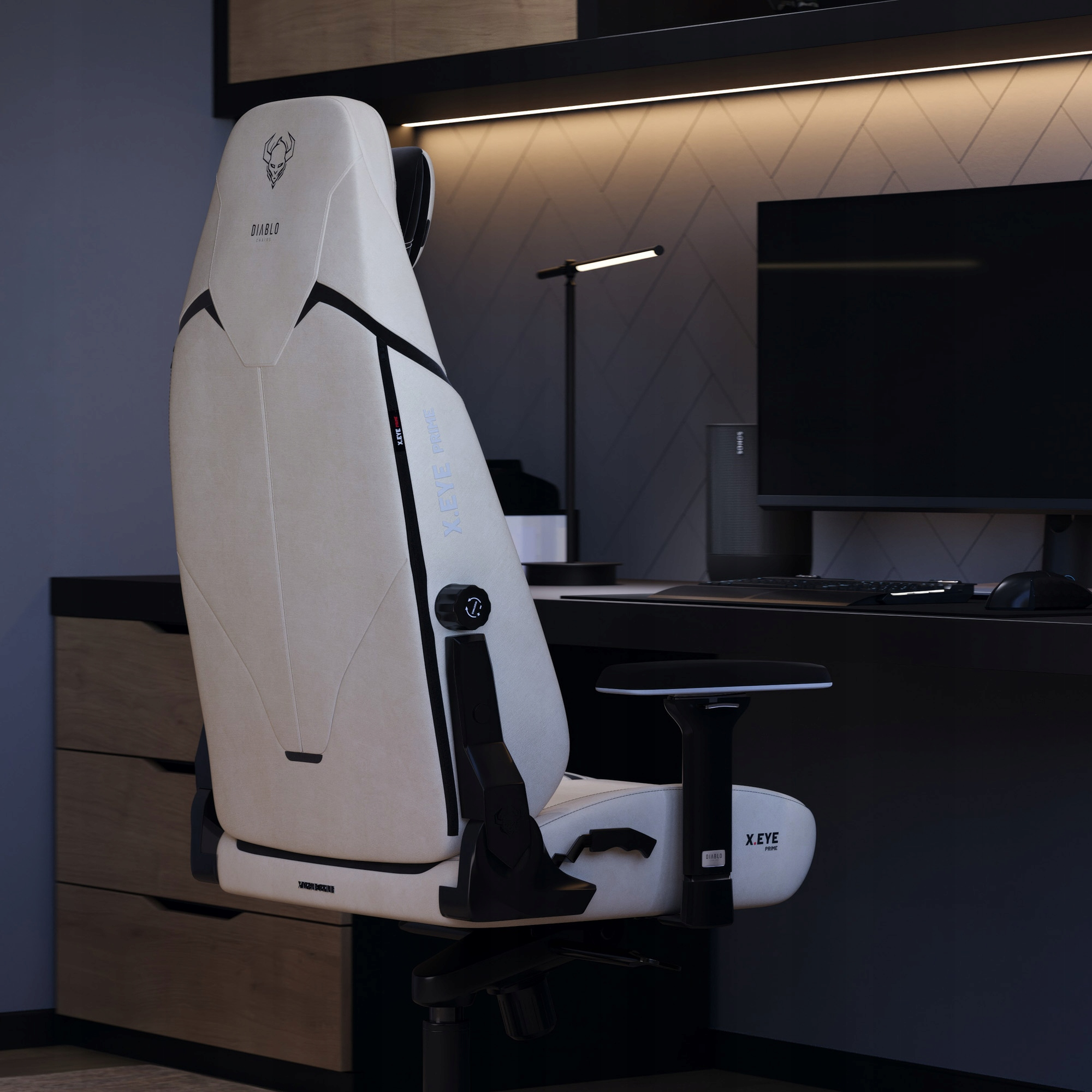 Biało-czarny fotel do gier w otoczeniu biurowym. Monitor, klawiatura i lampa znajdują się na biurku z tyłu.