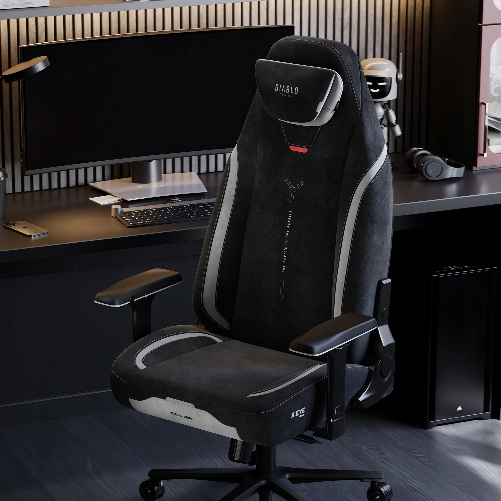 Czarny fotel gamingowy z białymi akcentami stoi przed biurkiem z monitorem, klawiaturą i akcesoriami. Widoczny jest robot i słuchawki.