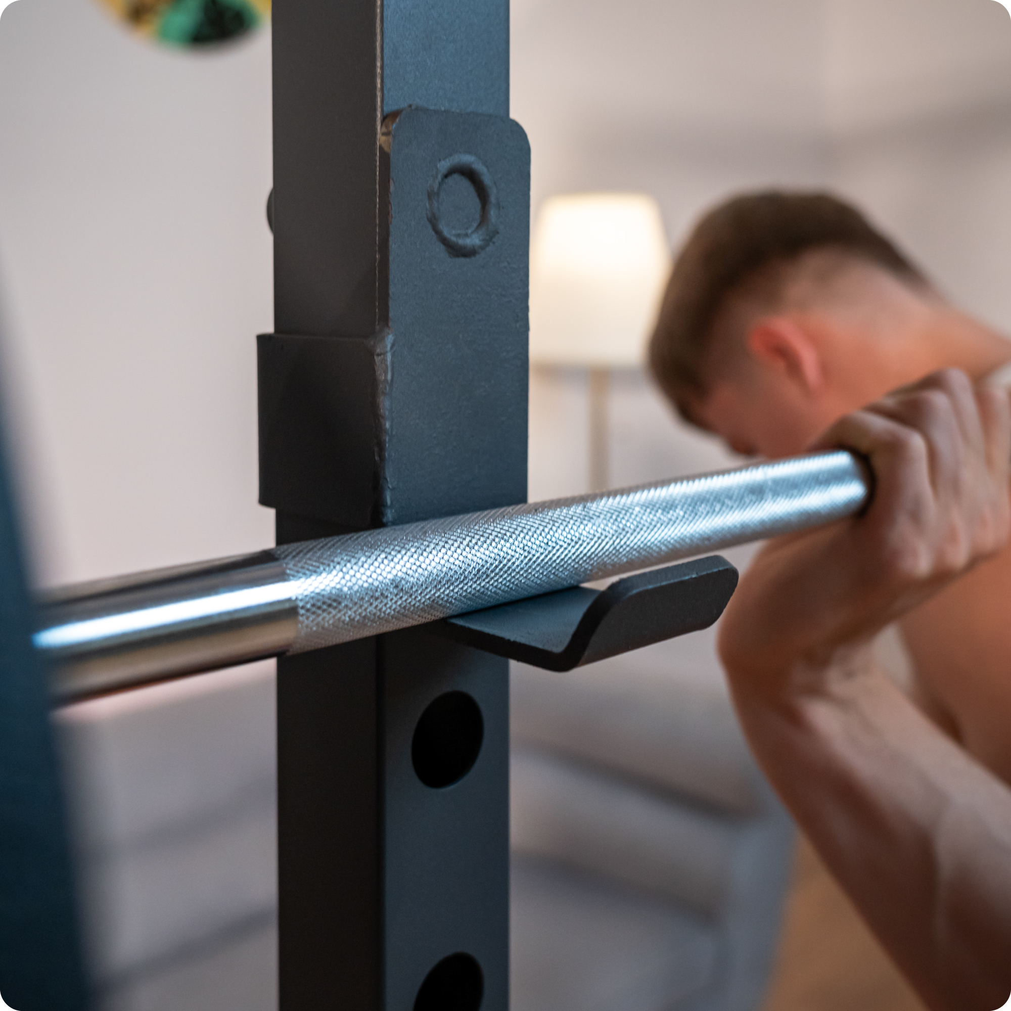 Osoba używająca sztangi na siłowni. Sztanga spoczywa na stojaku. Osoba jest w tle.