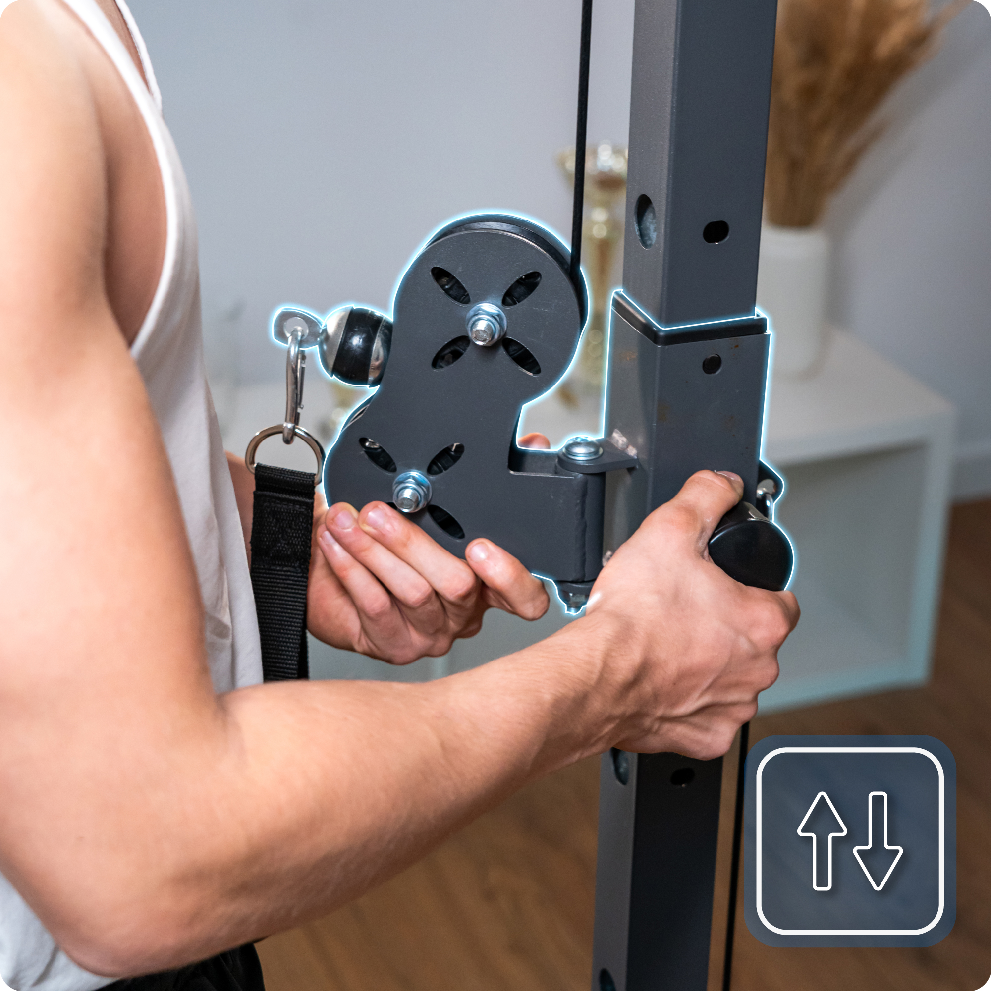 Osoba instaluje krążek linowy maszyny do ćwiczeń. Maszyna jest szara i czarna, z białą górą. Ikona pokazuje strzałki w górę i w dół.