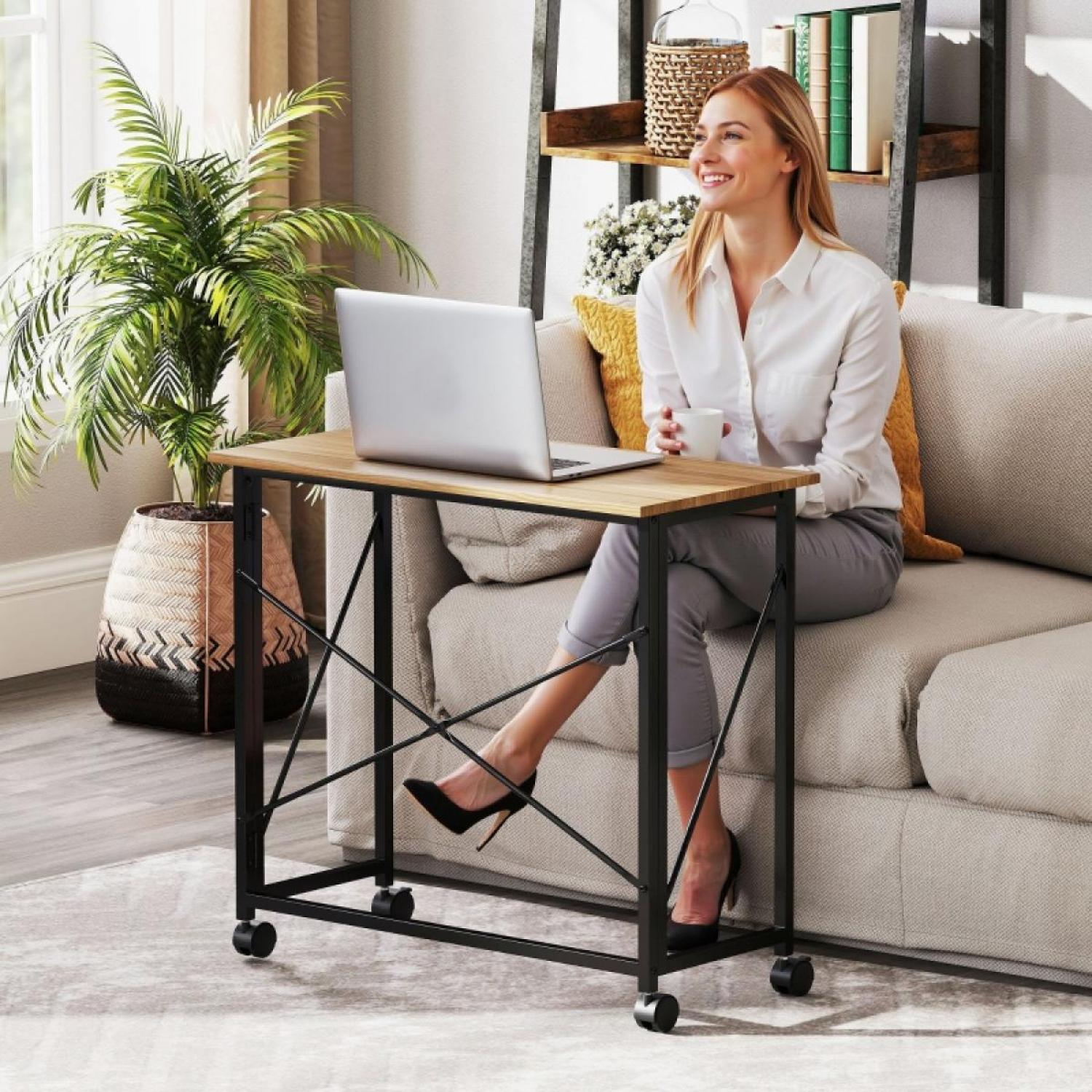 Eine Frau sitzt auf einem Sofa mit einem Laptop auf einem Tisch. Eine Pflanze, Regale und ein Teppich sind im Hintergrund.