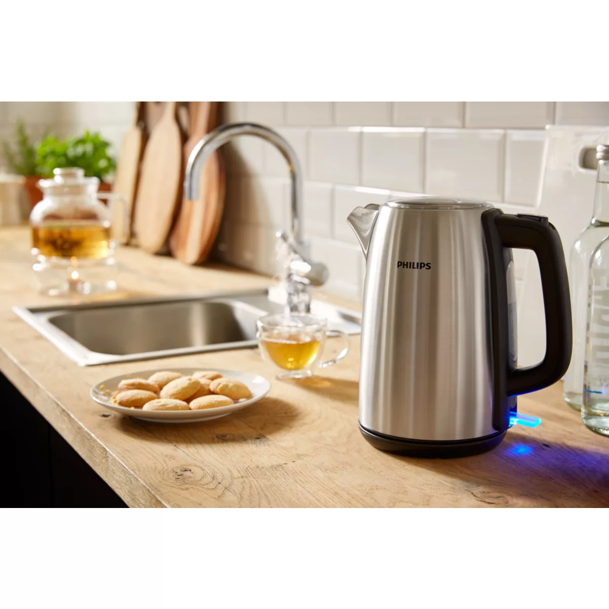 Küchenszene mit Philips-Kessel, Tee, Keksen und Spüle. Der Kessel ist silberfarben, mit schwarzem Griff. Kekse sind auf einem Teller.