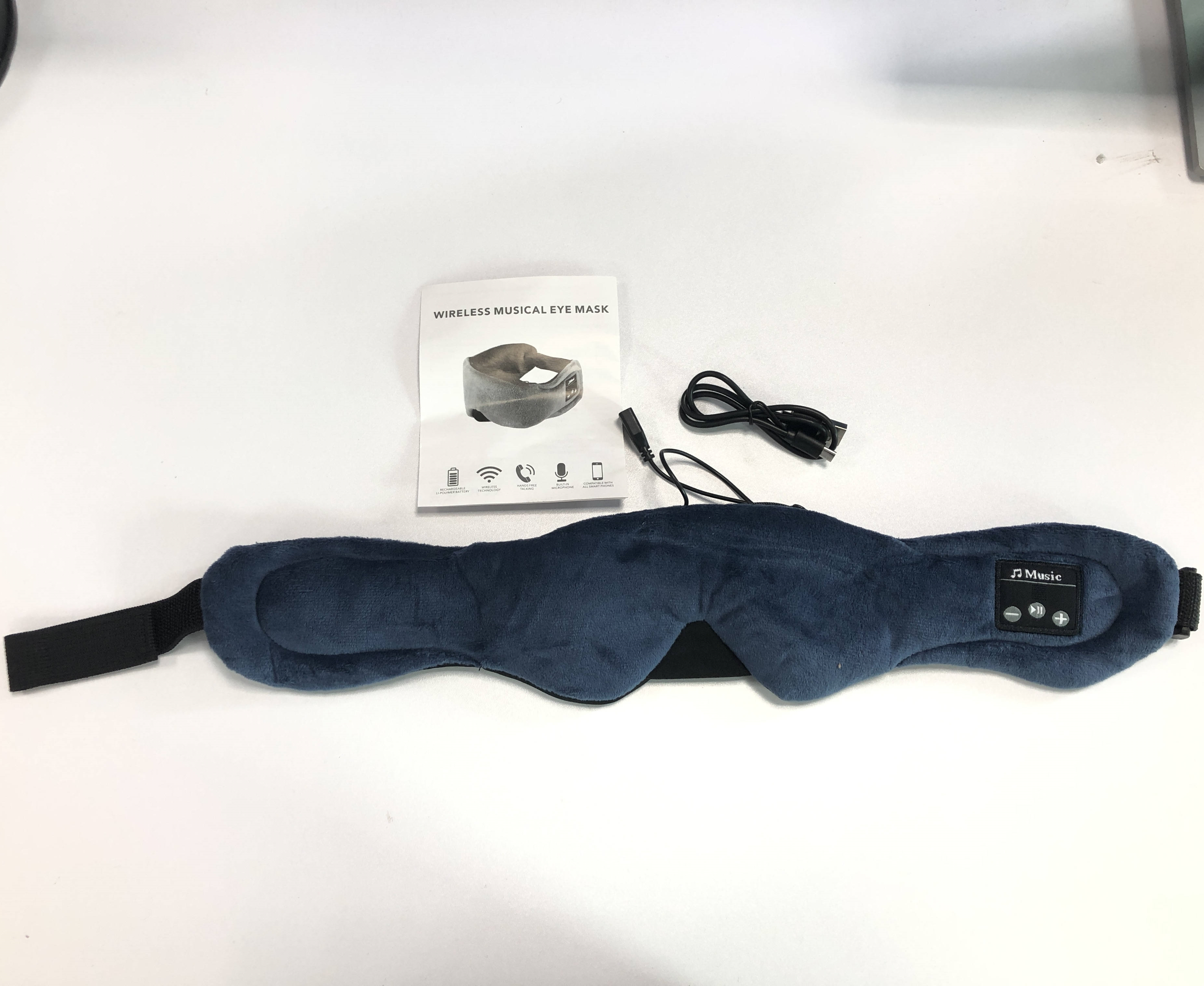 Eine blaue, kabellose, musikalische Augenmaske mit Bedienfeld, Broschüre, Ladekabel und weißem Hintergrund.