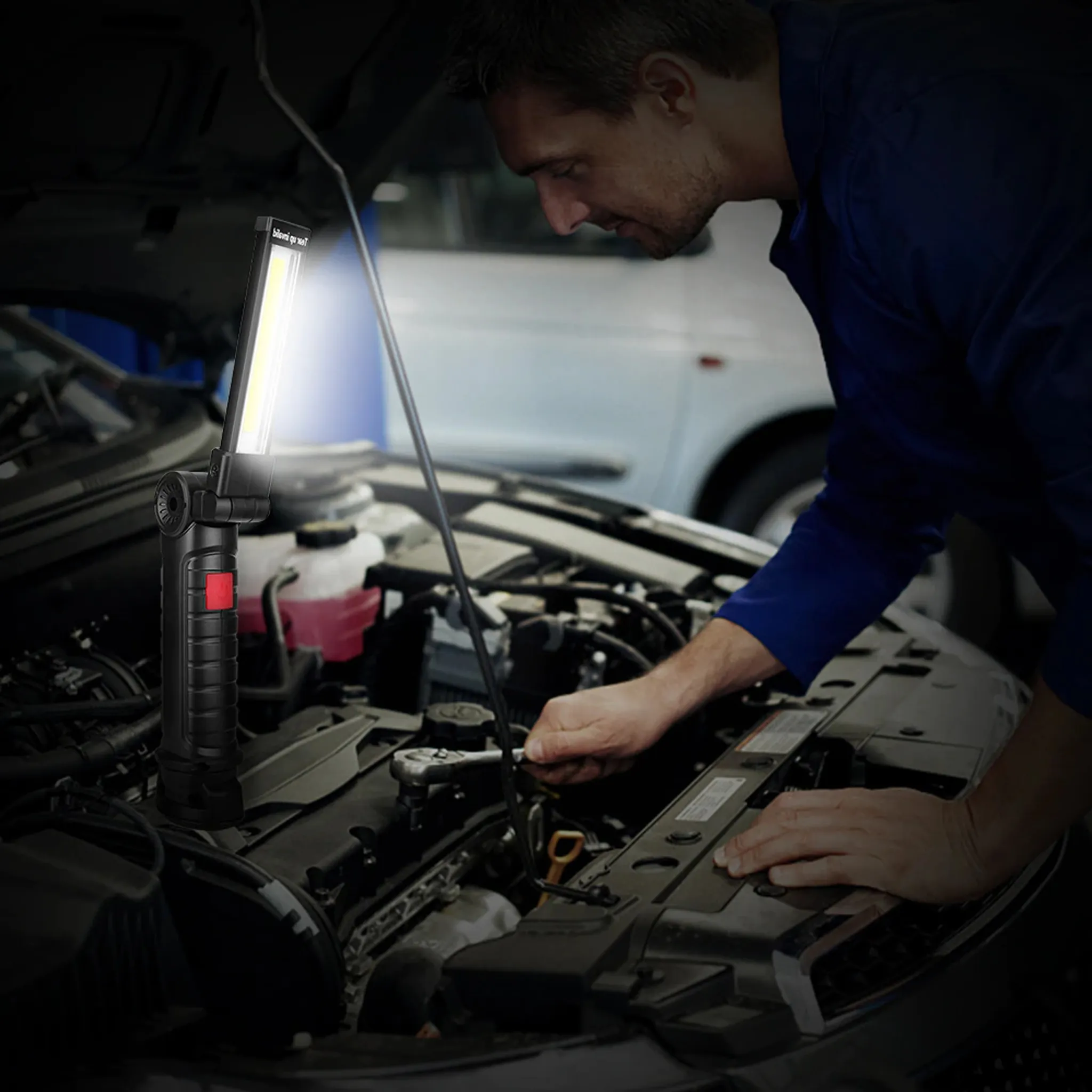 Ein Mann in blauem Hemd arbeitet an einem Automotor, beleuchtet von einer hellen LED-Arbeitsleuchte in seiner linken Hand.