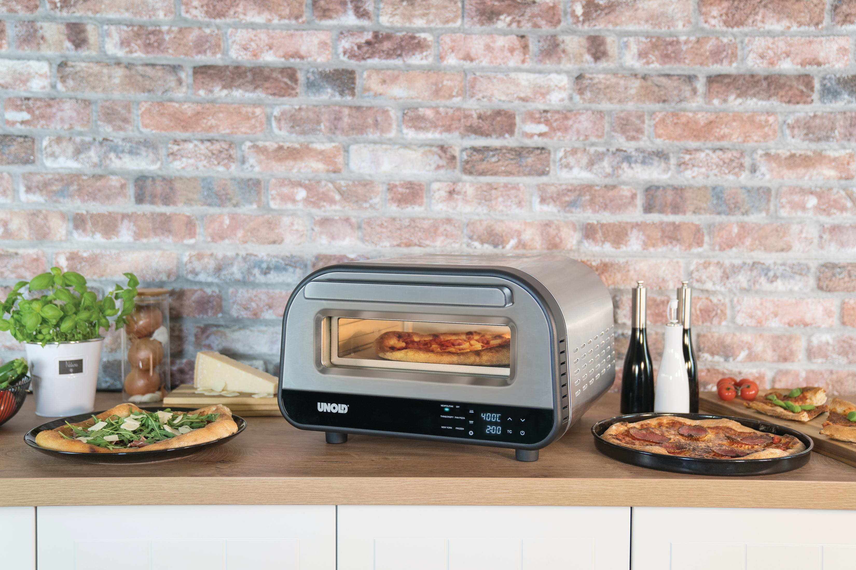 Un forno per pizza con pizza all'interno, su un bancone di legno. Pizza su piatti, erbe, formaggio e altri cibi sul bancone.
