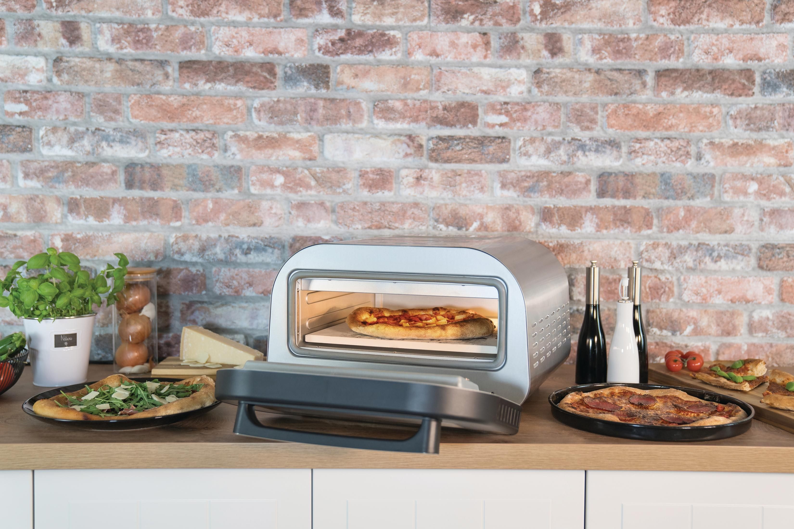 Un forno per pizza con una pizza all'interno. Altre pizze, ingredienti e bottiglie sono sul bancone, con un muro di mattoni sullo sfondo.