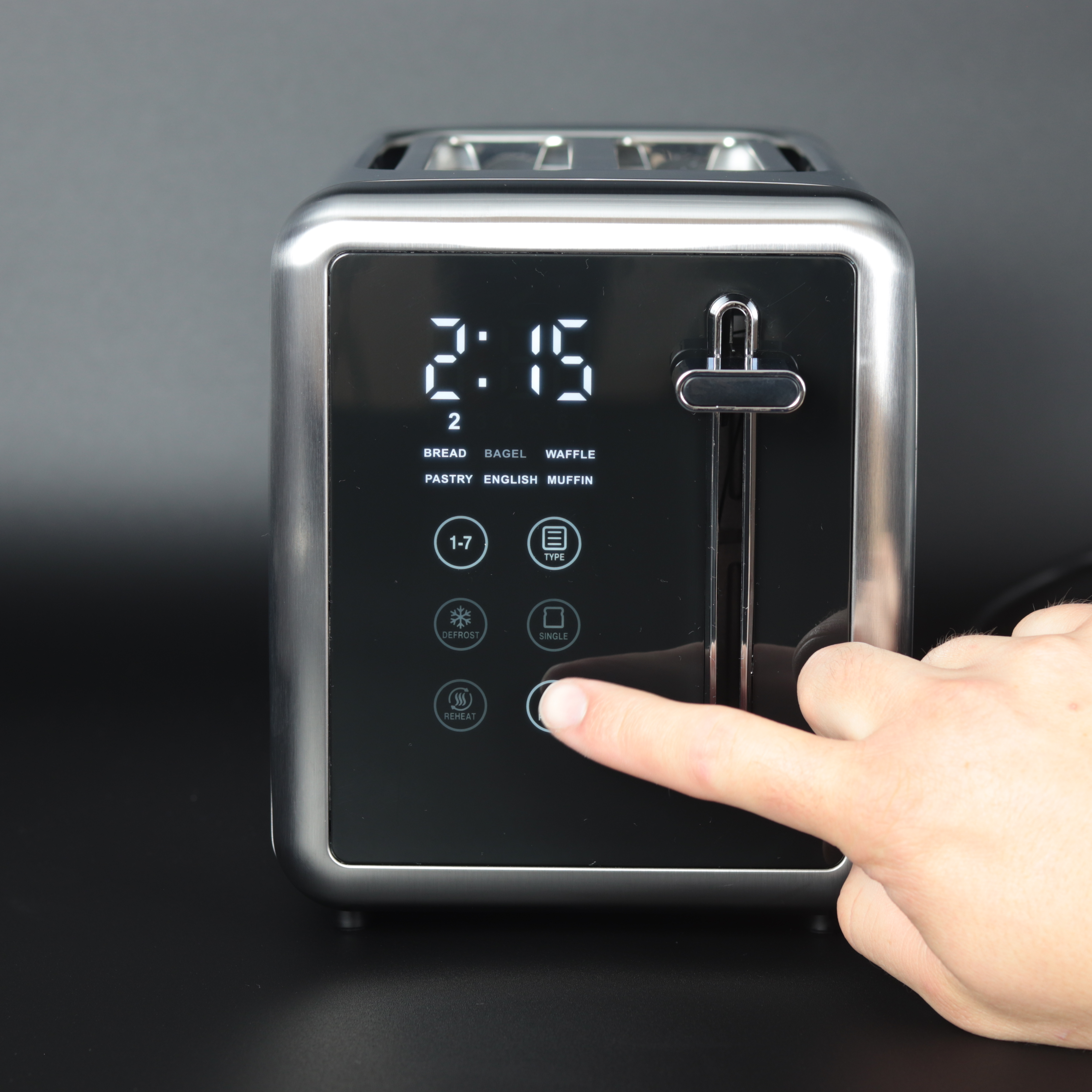 Eine Hand drückt eine Taste an einem silbernen Toaster. Das Display zeigt 2:15. Optionen für Brot werden angezeigt.