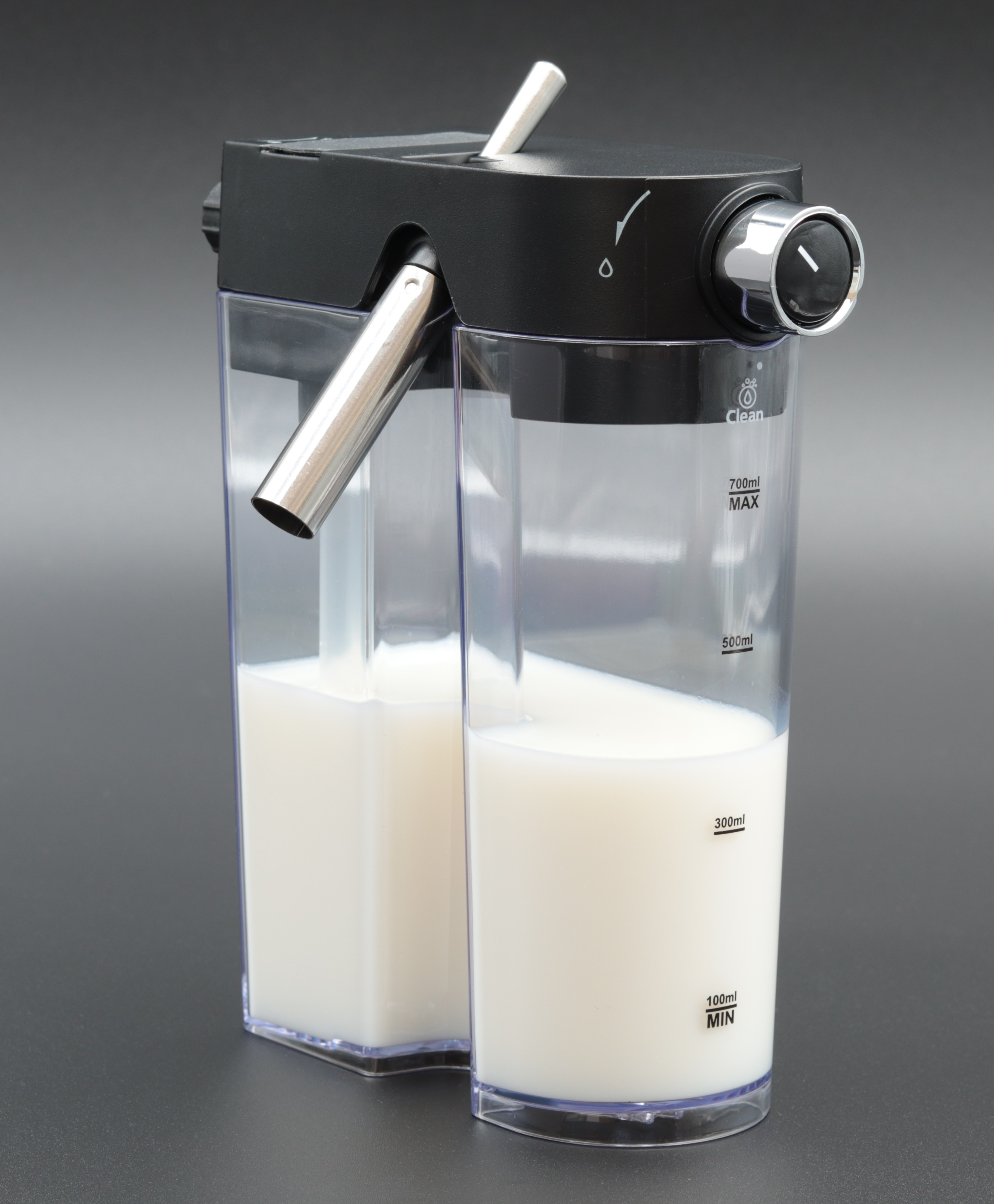 Ein Milchaufschäumer mit zwei durchsichtigen Behältern, die mit Milch gefüllt sind. Schwarze Oberseite mit silberner Düse und Knopf. Grauer Hintergrund.