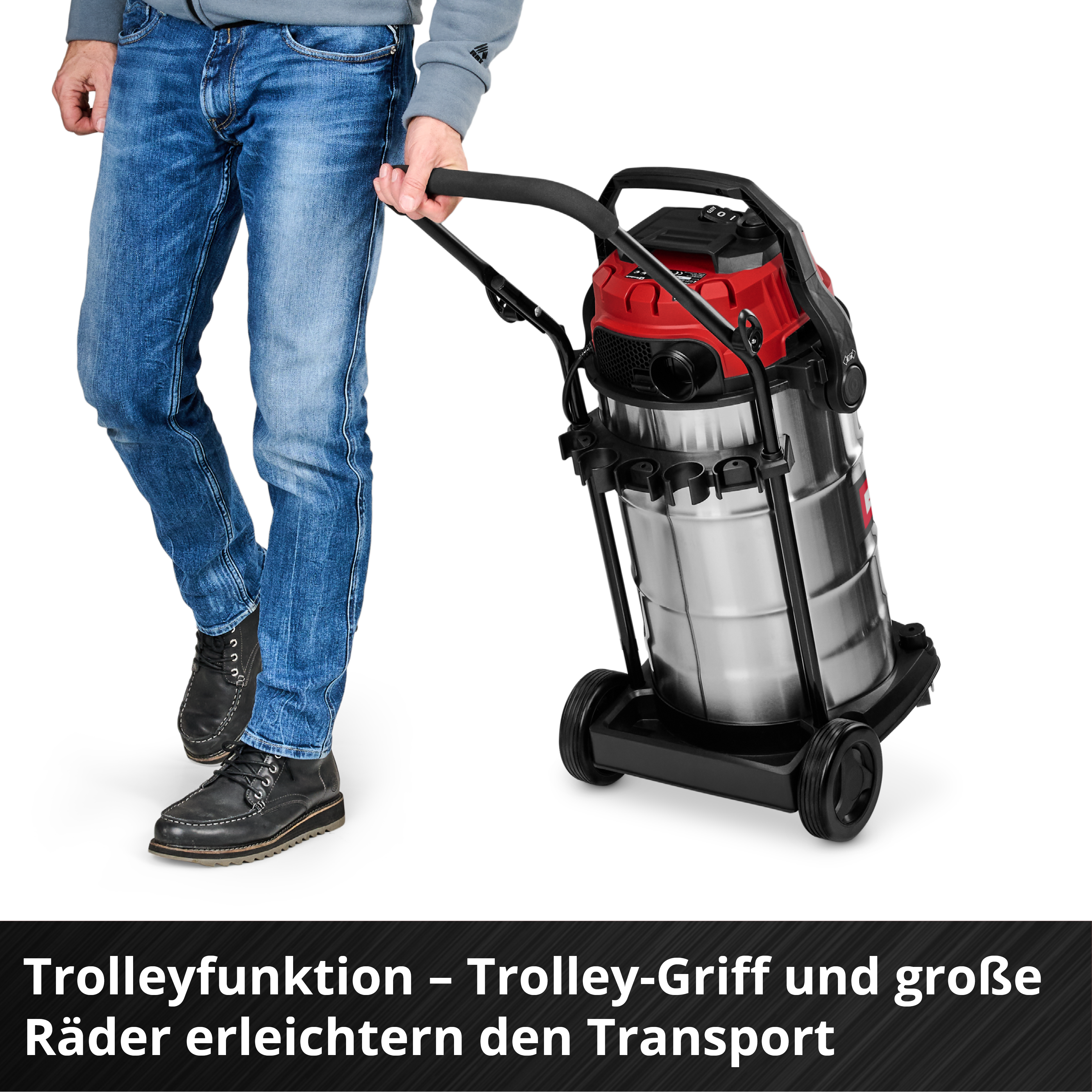 Ein Mann zieht einen roten und silbernen Staubsauger auf Rädern. Er trägt Jeans und schwarze Schuhe.