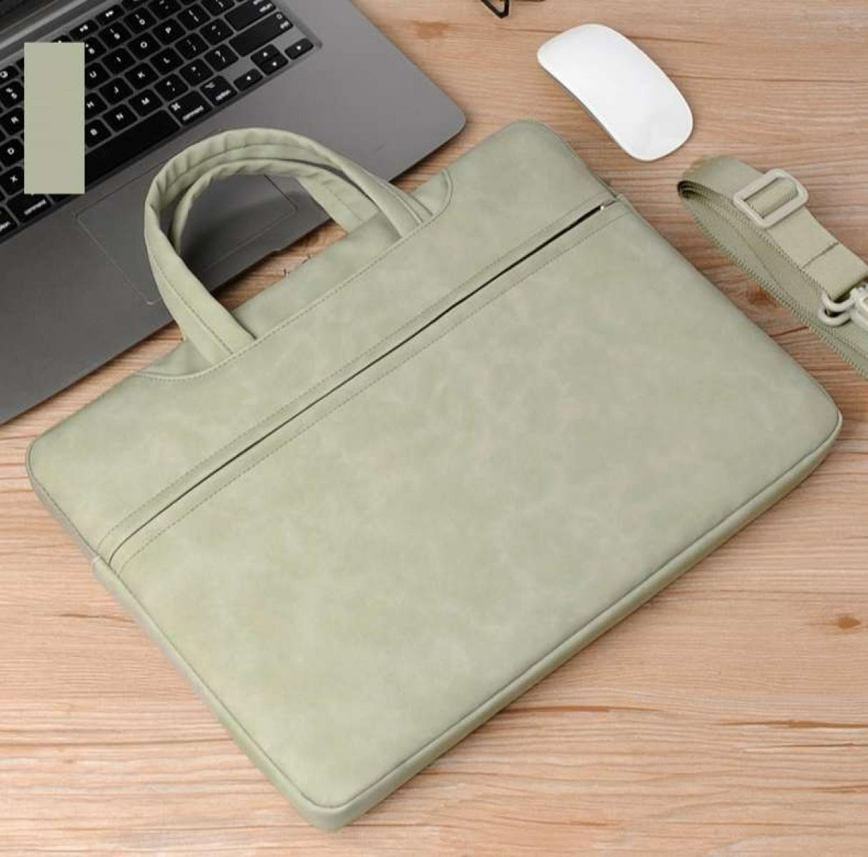 Eine hellgrüne Laptoptasche mit Reißverschluss liegt auf einer Holzoberfläche. Ein Laptop, eine Maus und ein Gurt sind ebenfalls vorhanden.