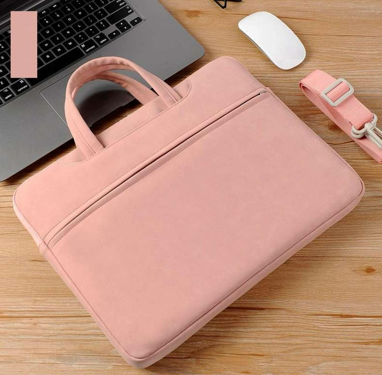 Eine rosa Laptoptasche mit Griffen und Schultergurt liegt auf einer Holzoberfläche, neben einem Laptop und einer weißen Maus.