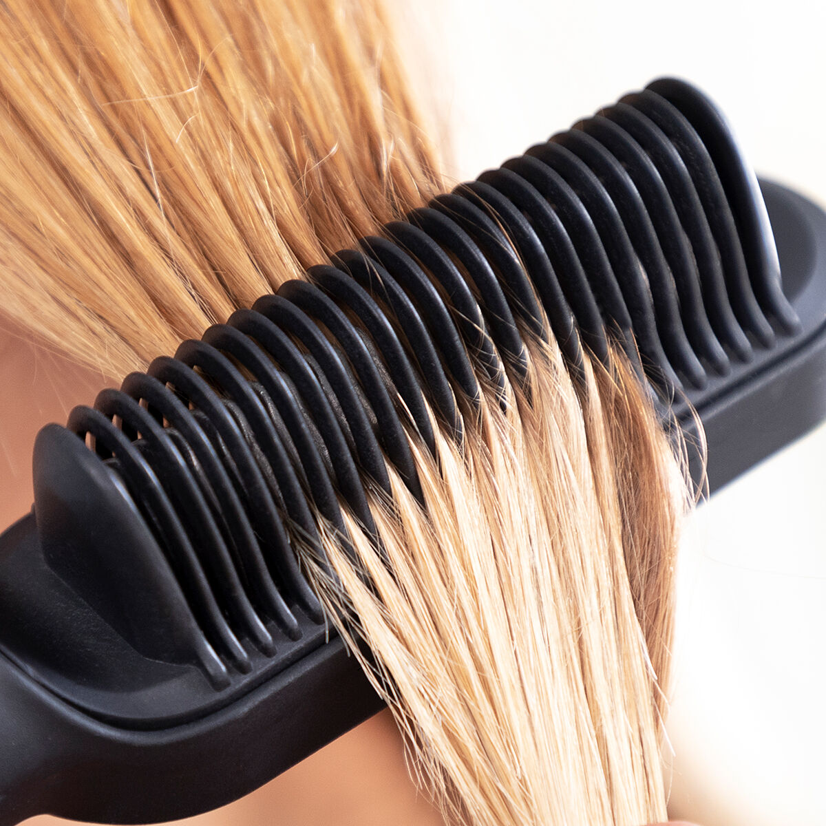 Ein schwarzer Haarglätter wird auf blondem Haar verwendet. Der Kamm steht im Fokus, das Haar fließt hindurch.