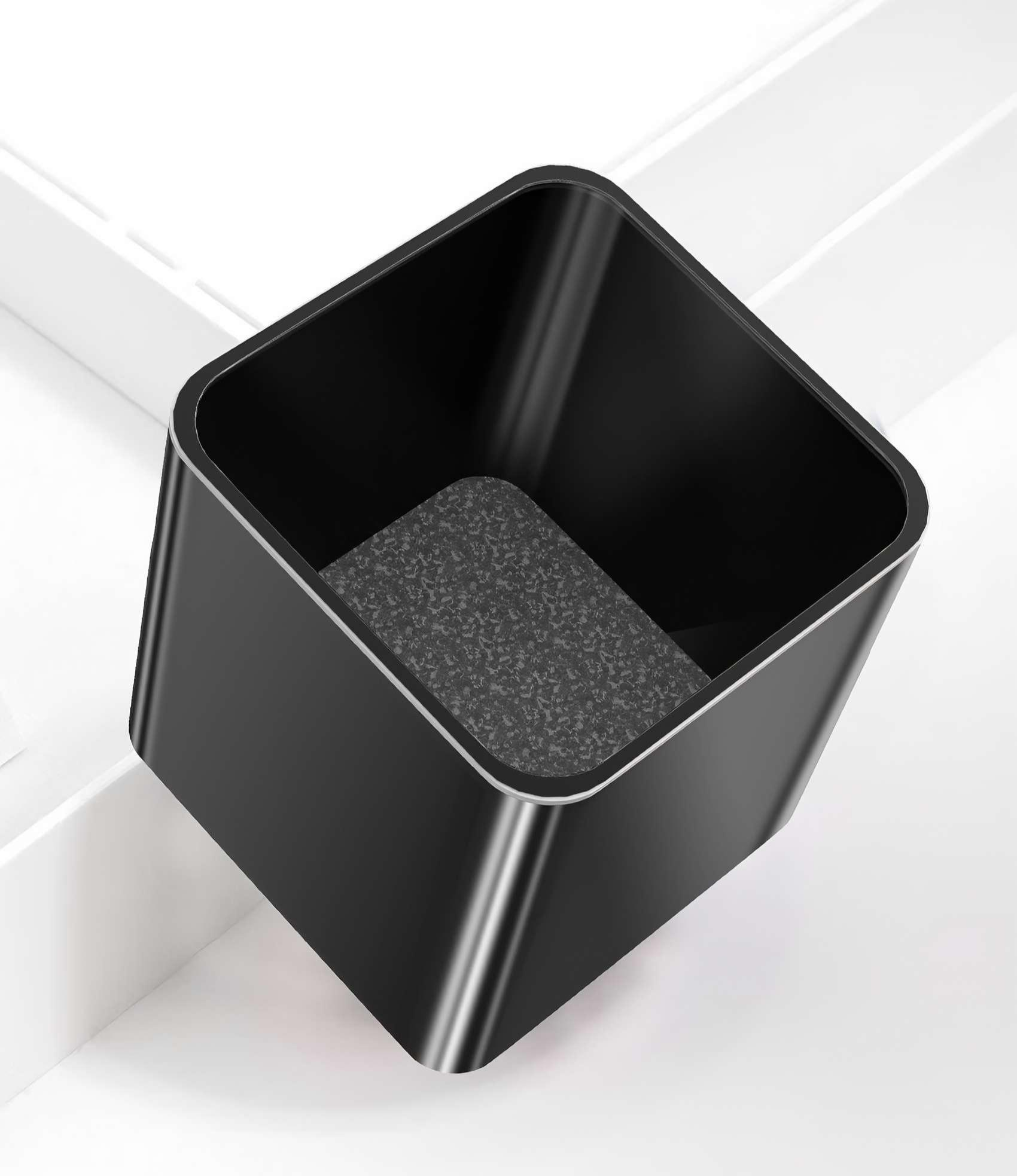 Ein schwarzer quadratischer Behälter mit strukturierter Basis steht schräg auf einer weißen Oberfläche, mit weißem Hintergrund.