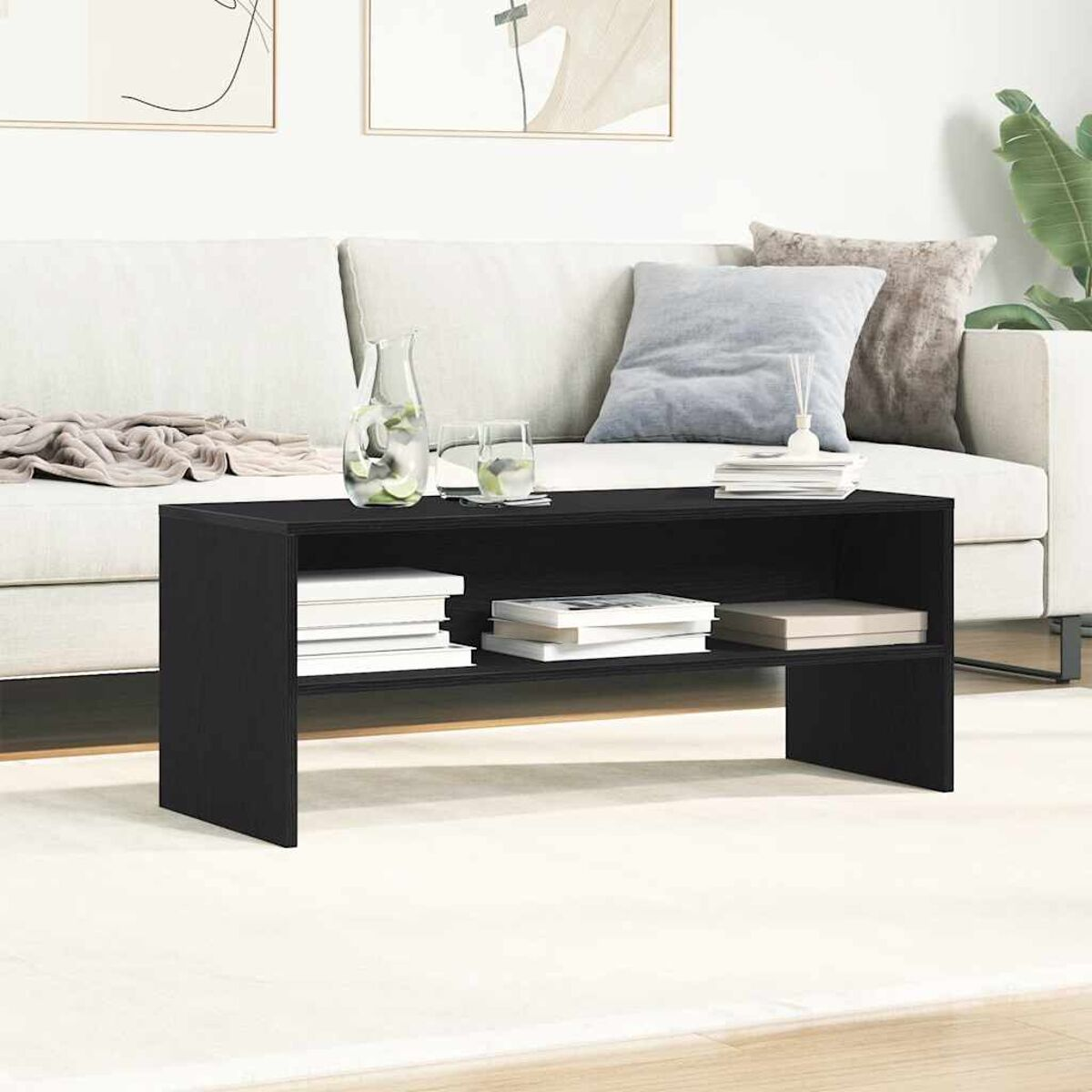 Ein schwarzer Couchtisch mit Büchern und Gläsern darauf. Eine weiße Couch und ein Teppich sind im Hintergrund.