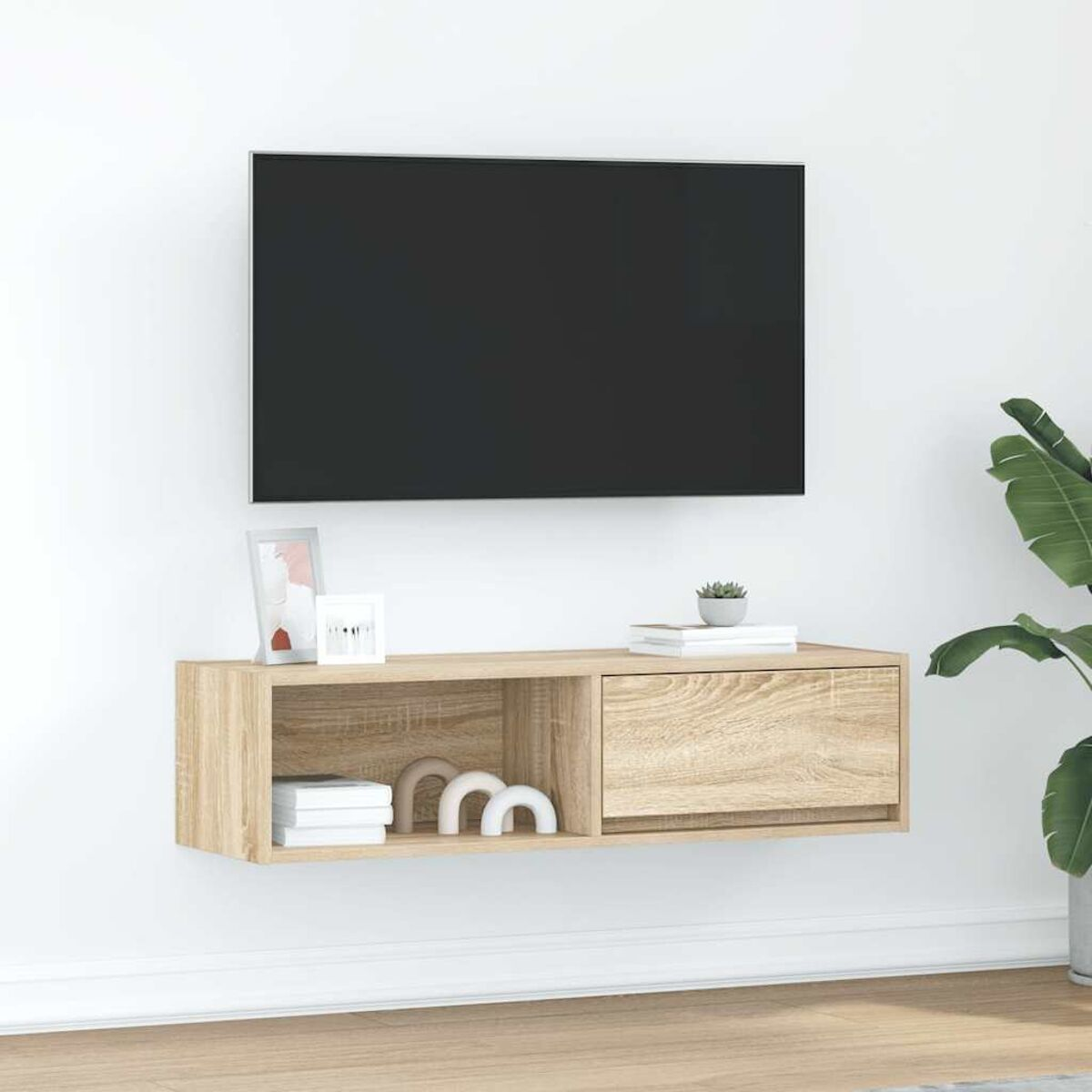 Ein an der Wand montierter Fernseher über einem Holzschrank. Rechts ist eine Pflanze. Der Schrank hat eine Schublade, Bücher und Dekorationsartikel.