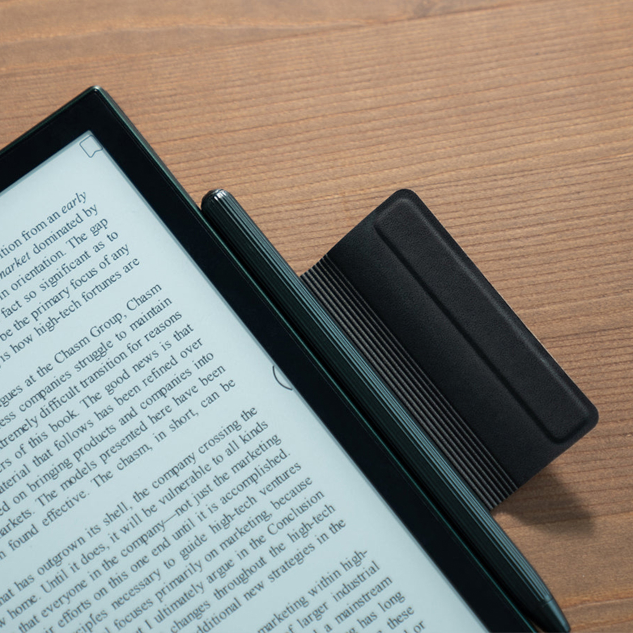 Ein E-Reader mit Text, Stift und schwarzer Hülle auf Holzoberfläche.