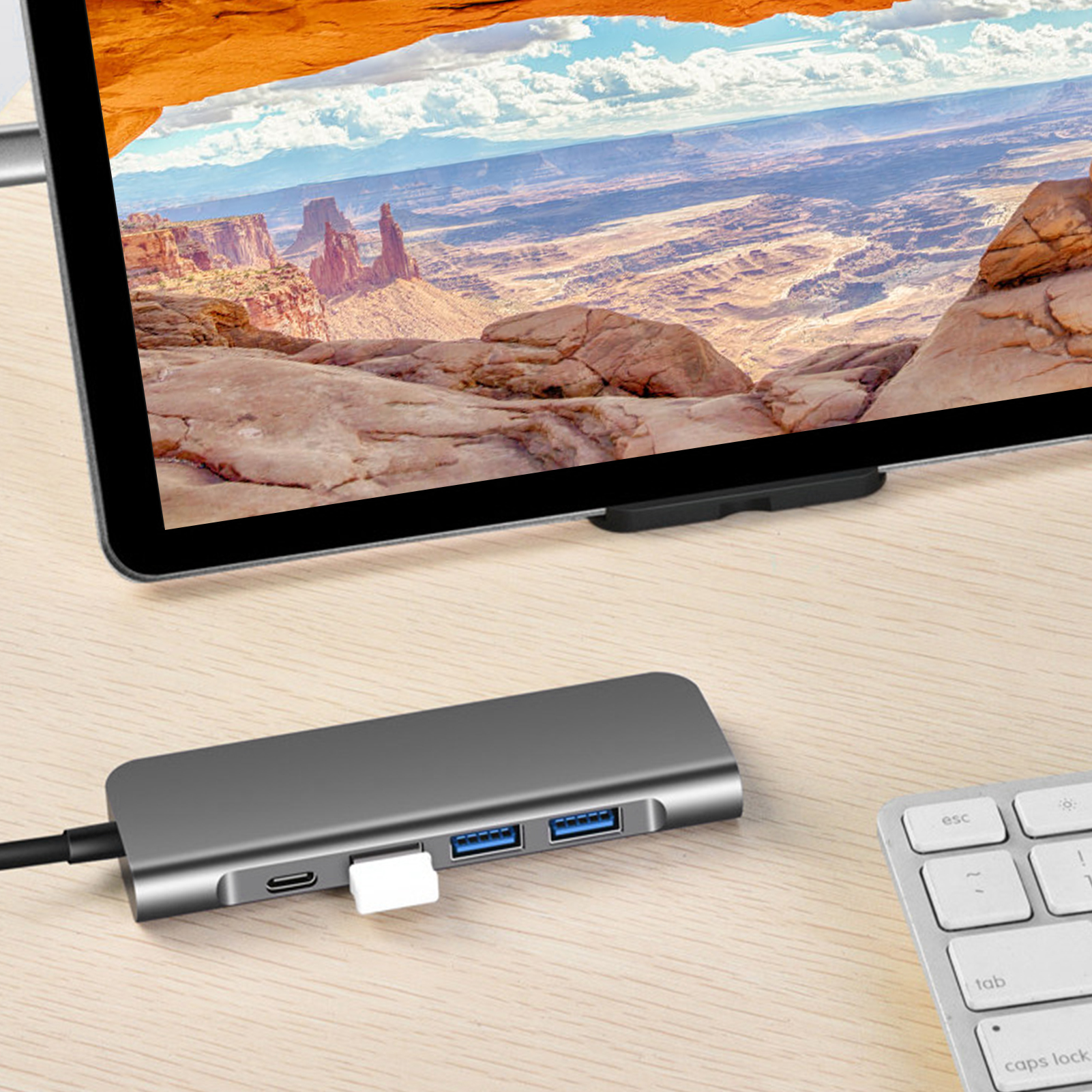 Ein Tablet zeigt eine Wüstenlandschaft. Darunter liegt ein USB-Hub mit angeschlossenem USB-Laufwerk auf einem Holztisch, neben einer Tastatur.
