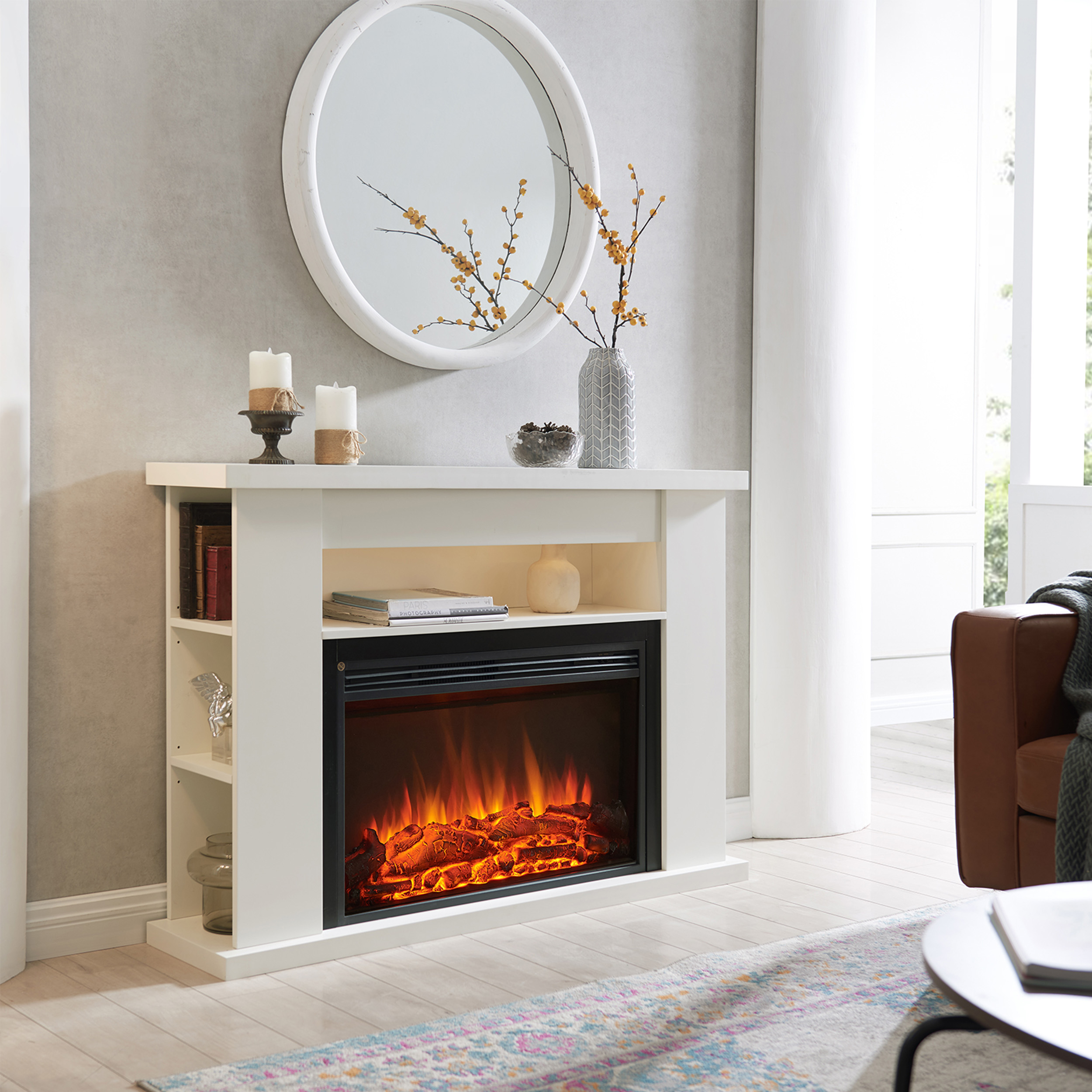 Ein weißer Kamin mit Flammeneffekt, Kerzen und einem Spiegel. Ein braunes Ledersofa und ein Teppich sind ebenfalls sichtbar.