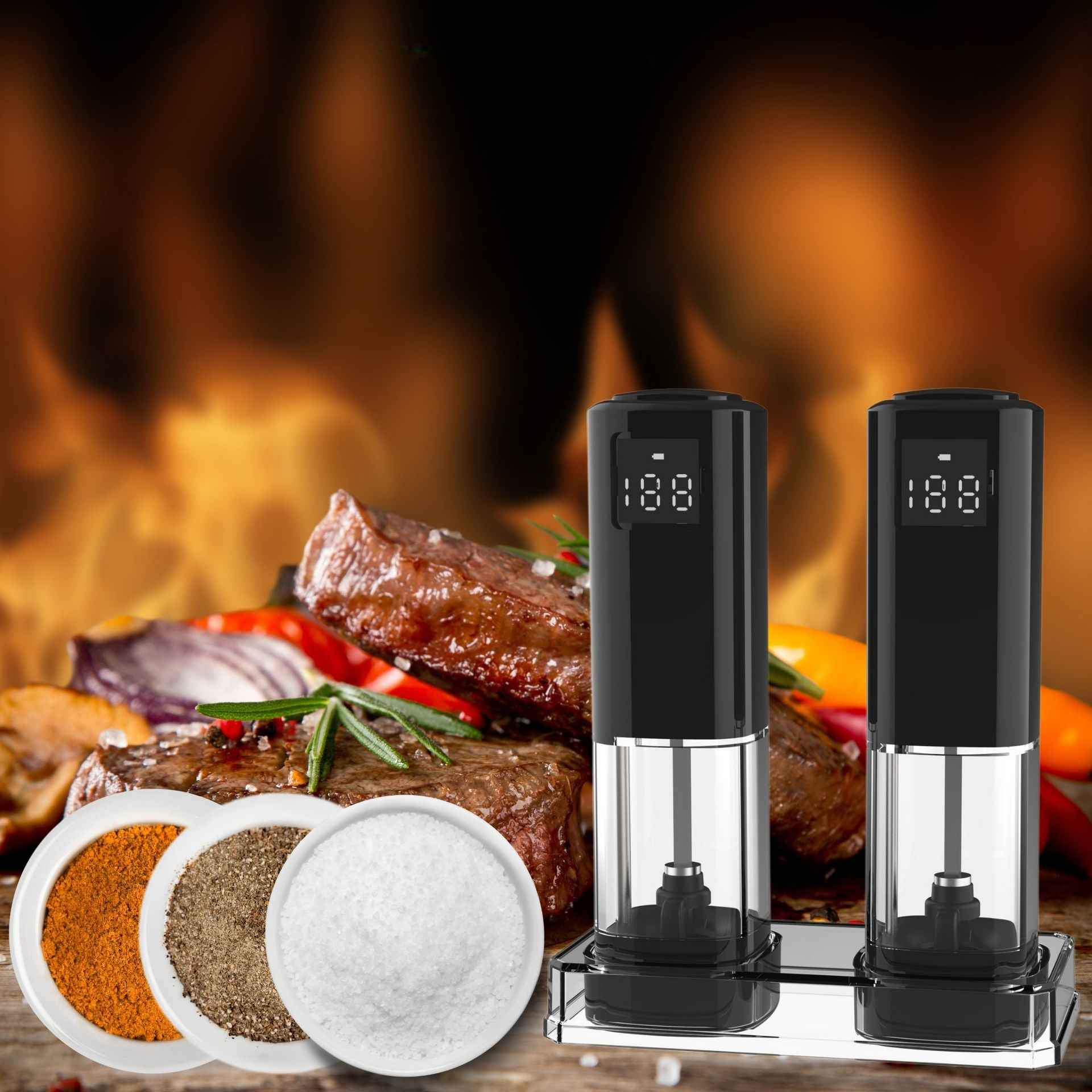 Zwei schwarze elektrische Salz- und Pfeffermühlen mit Digitalanzeigen, Steak, Gewürze und Feuer im Hintergrund.