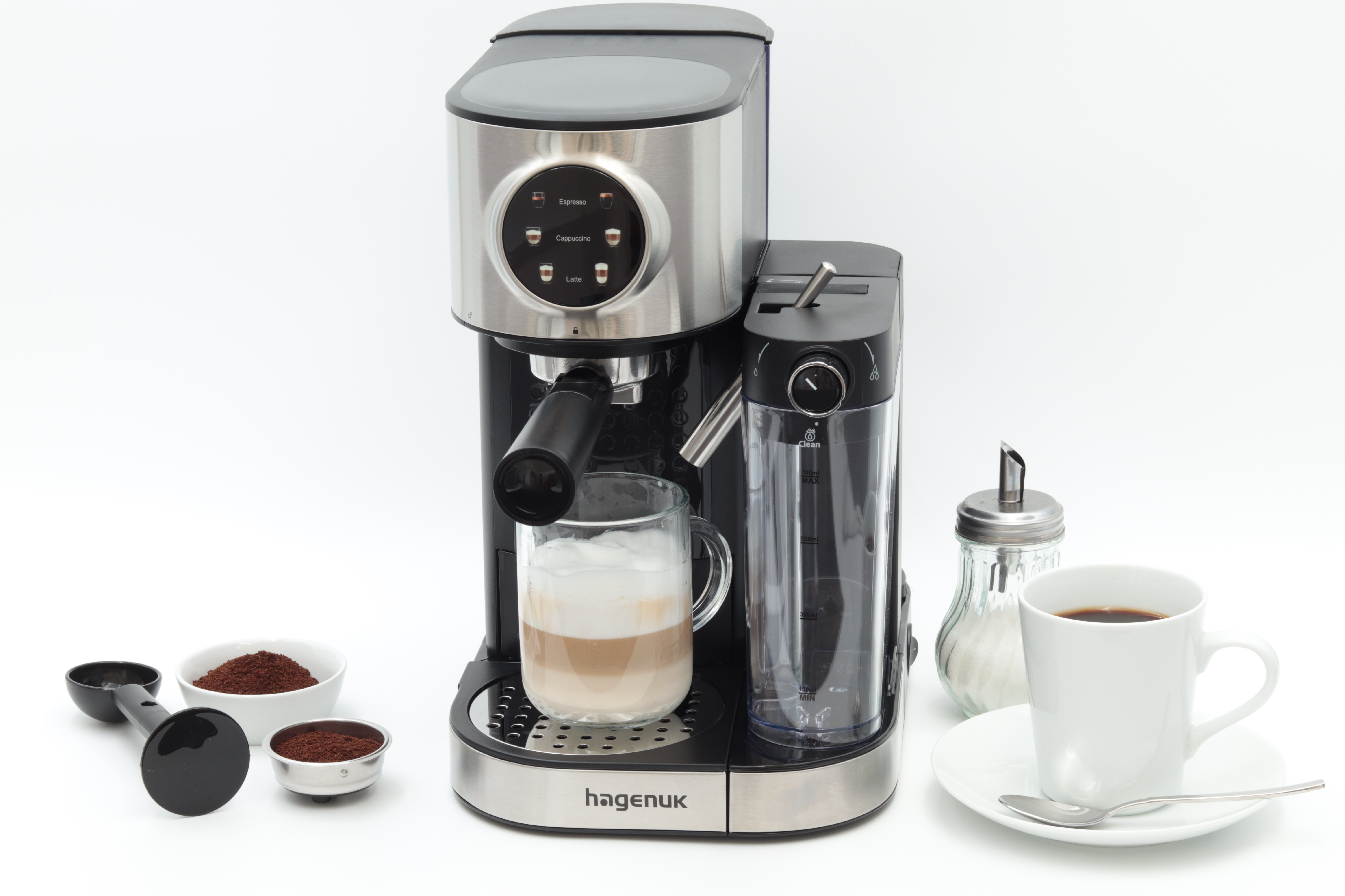 Kaffeemaschine mit einem Glas Latte, einer Tasse Kaffee, Zuckerdose, Kaffeepulver und Löffel auf weißer Oberfläche.
