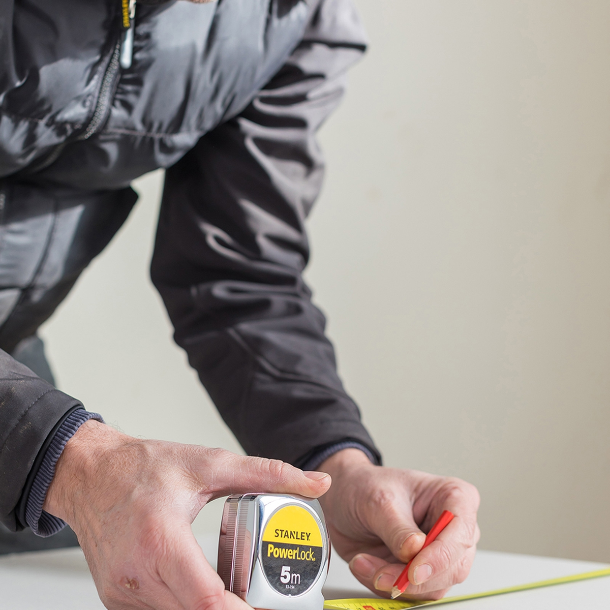 Osoba mierzy taśmą mierniczą Stanley PowerLock na białej powierzchni, używając czerwonego ołówka do zaznaczania.