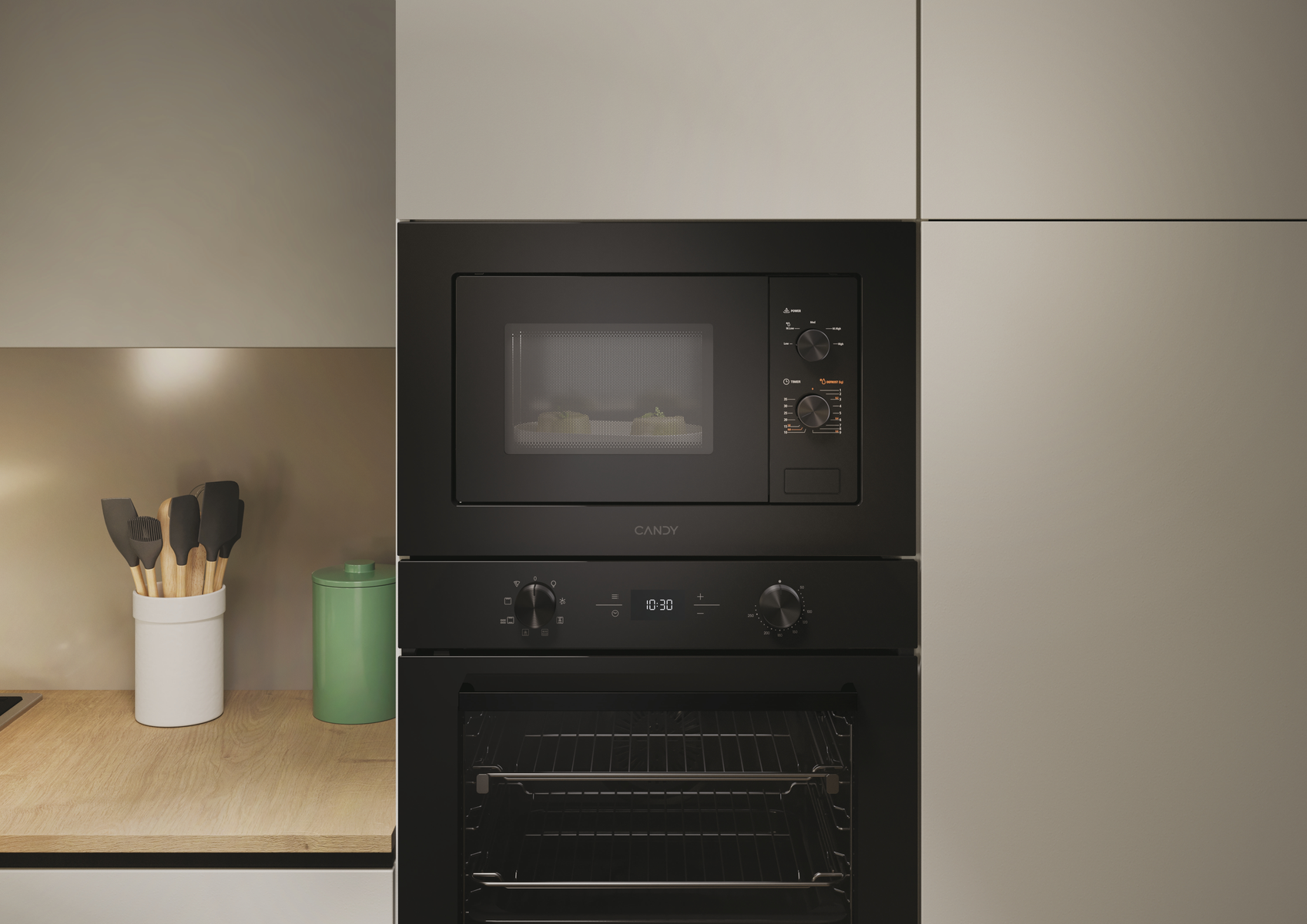 Un forno a microonde e un forno neri sono integrati in un mobile da cucina. Un barattolo bianco con utensili e un barattolo verde sono sul bancone.
