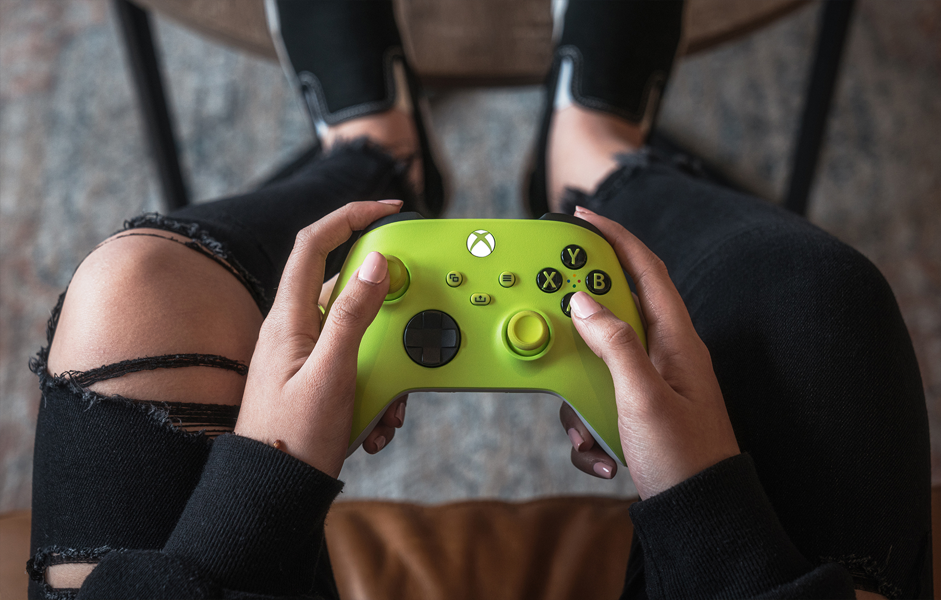 Eine Person hält einen limettengrünen Xbox-Controller. Die Person trägt eine schwarze Jeans und schwarze Schuhe. Der Hintergrund ist verschwommen.
