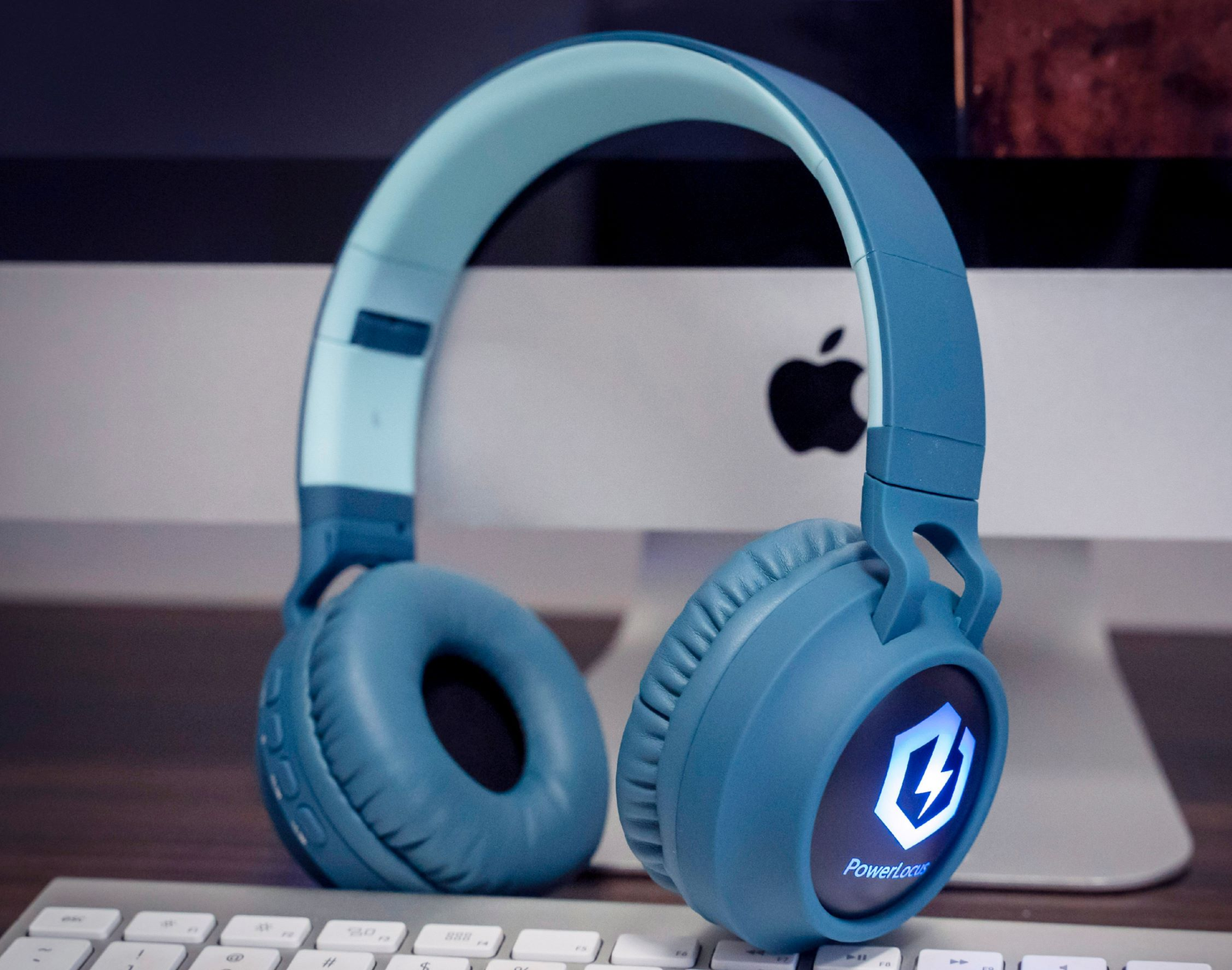 Cuffie blu su una scrivania con tastiera e computer sullo sfondo. Le cuffie hanno un logo che dice PowerLocus.
